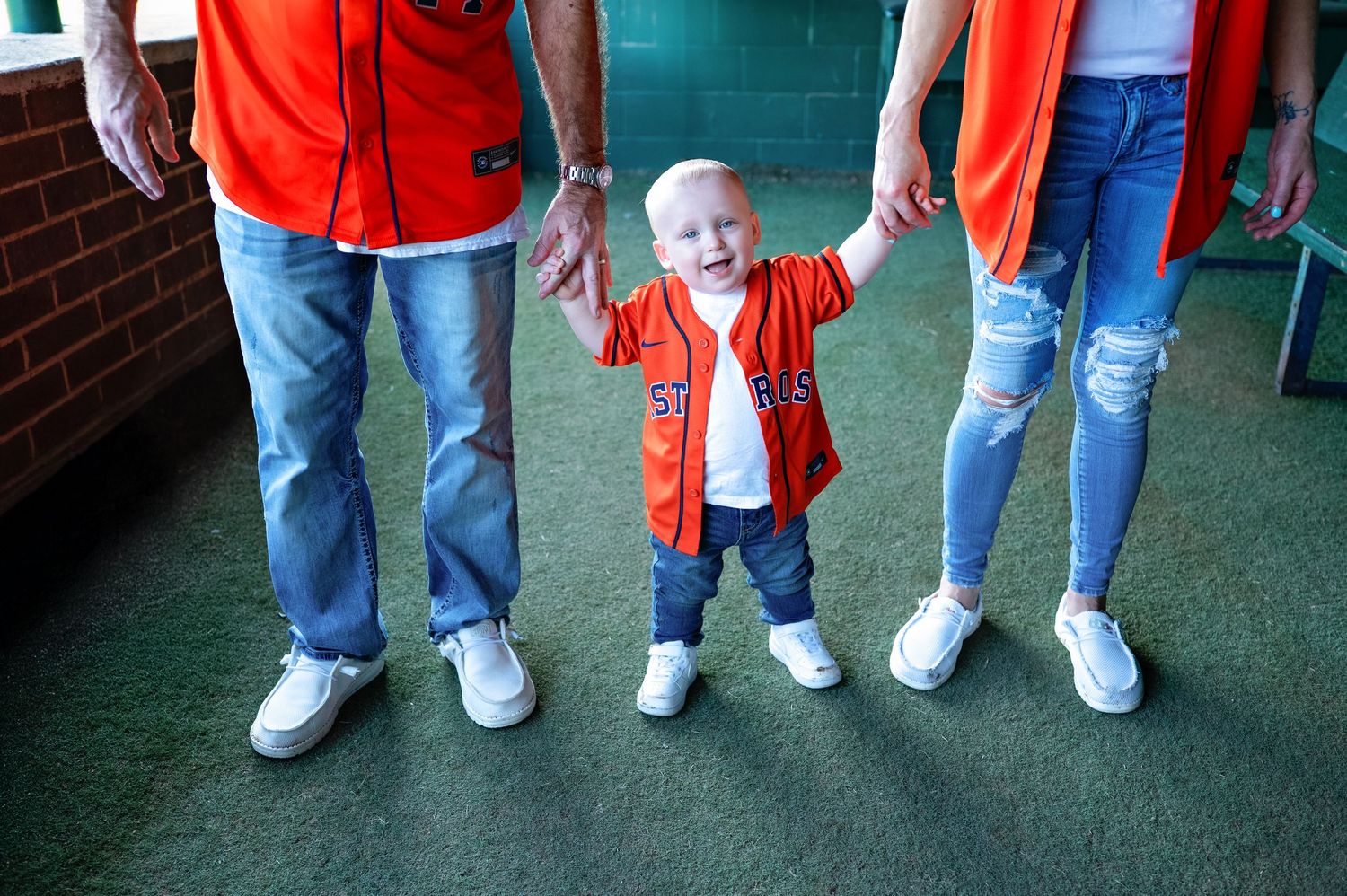 People wearing jeans and orange shirts stand in a row showing off their white sneakers on a tiled floor.
