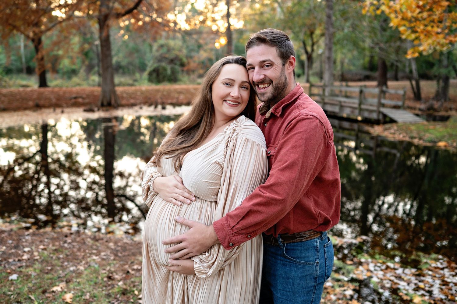 Couple in casual fall attire embracing outdoors during golden hour with autumn foliage in the background.