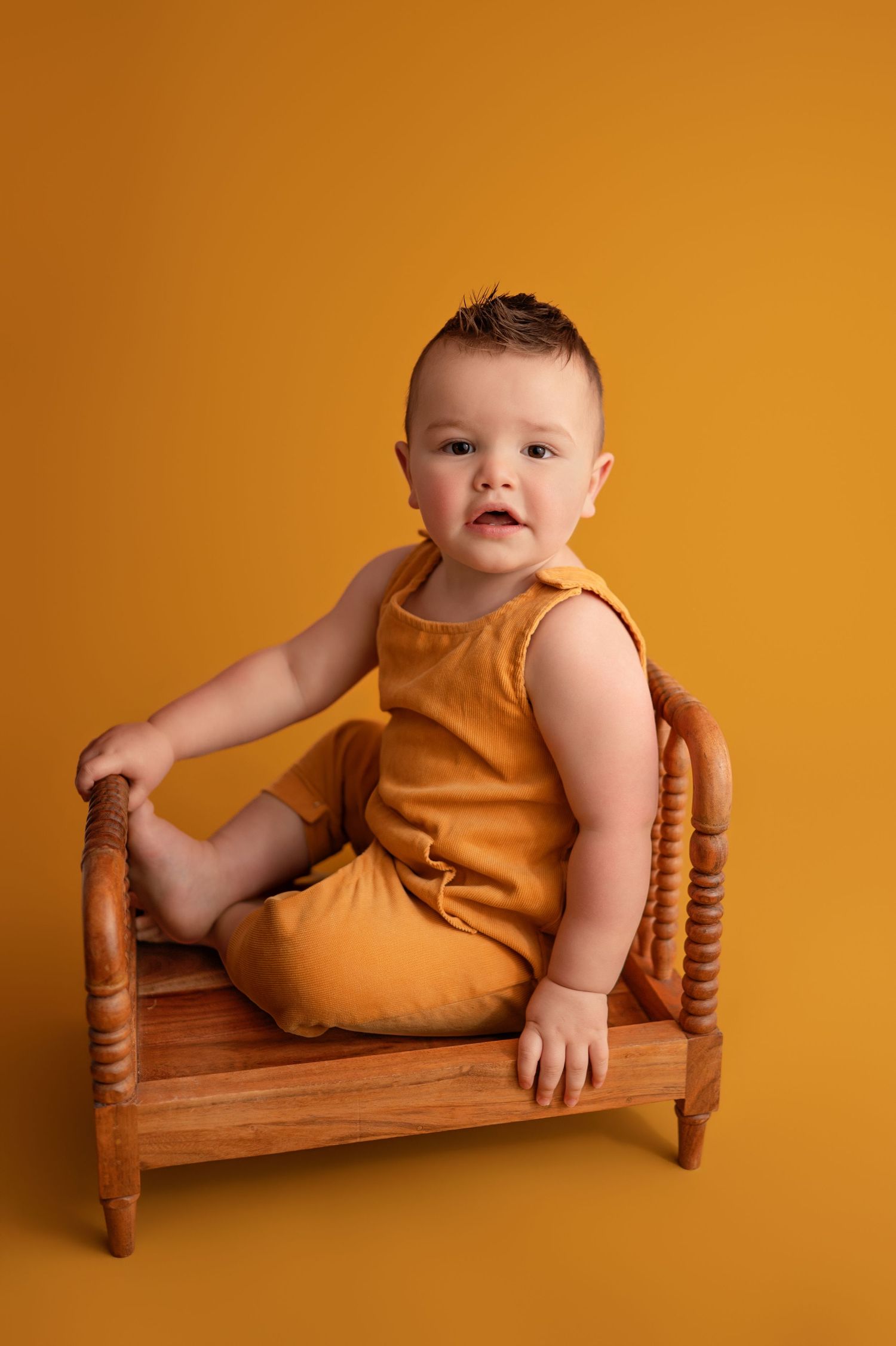Baby in orange romper poses on wooden bench against matching orange backdrop in progression of playful positions.