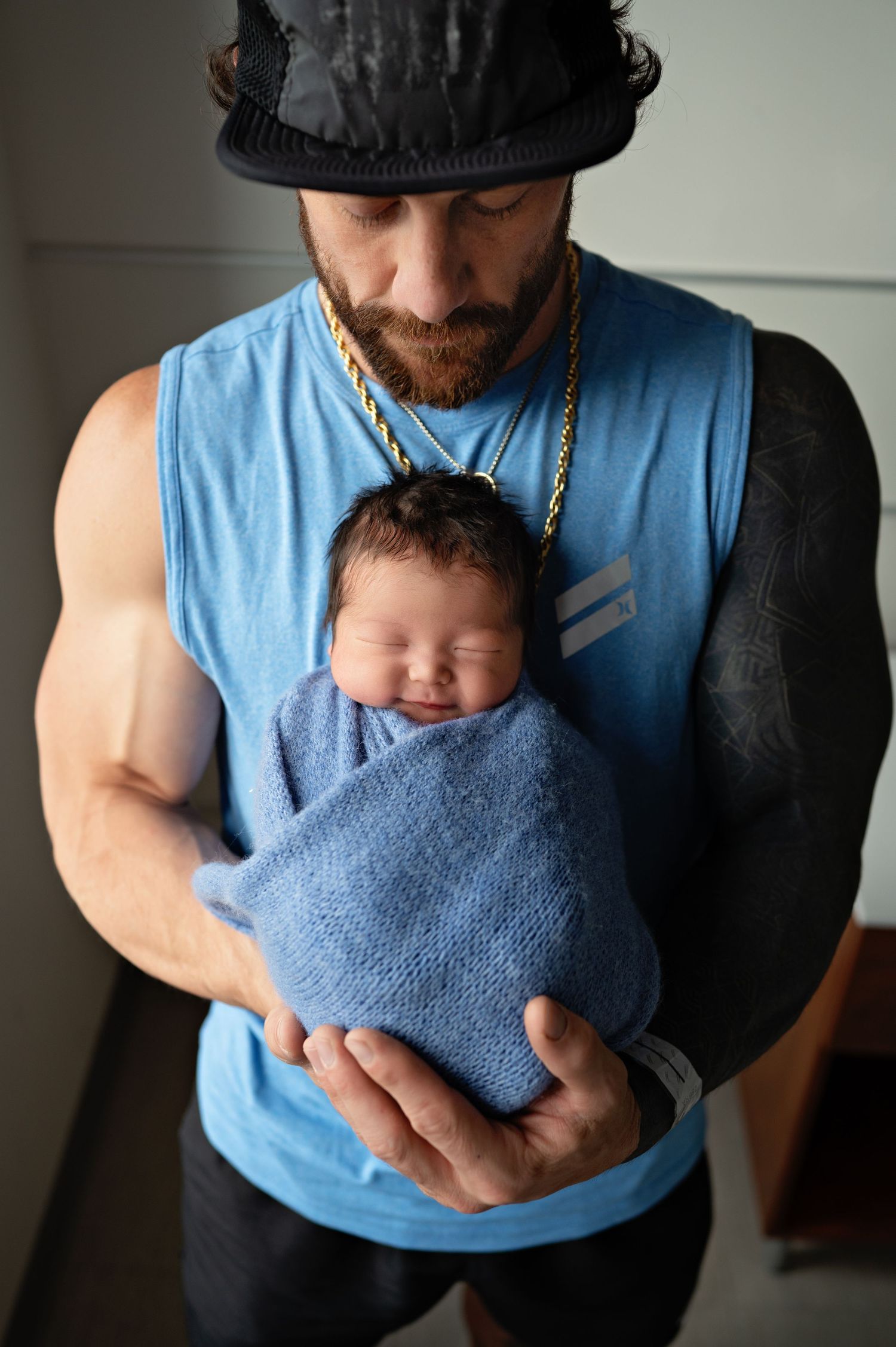 A newborn baby wrapped in a soft blue blanket is held gently while sleeping peacefully.