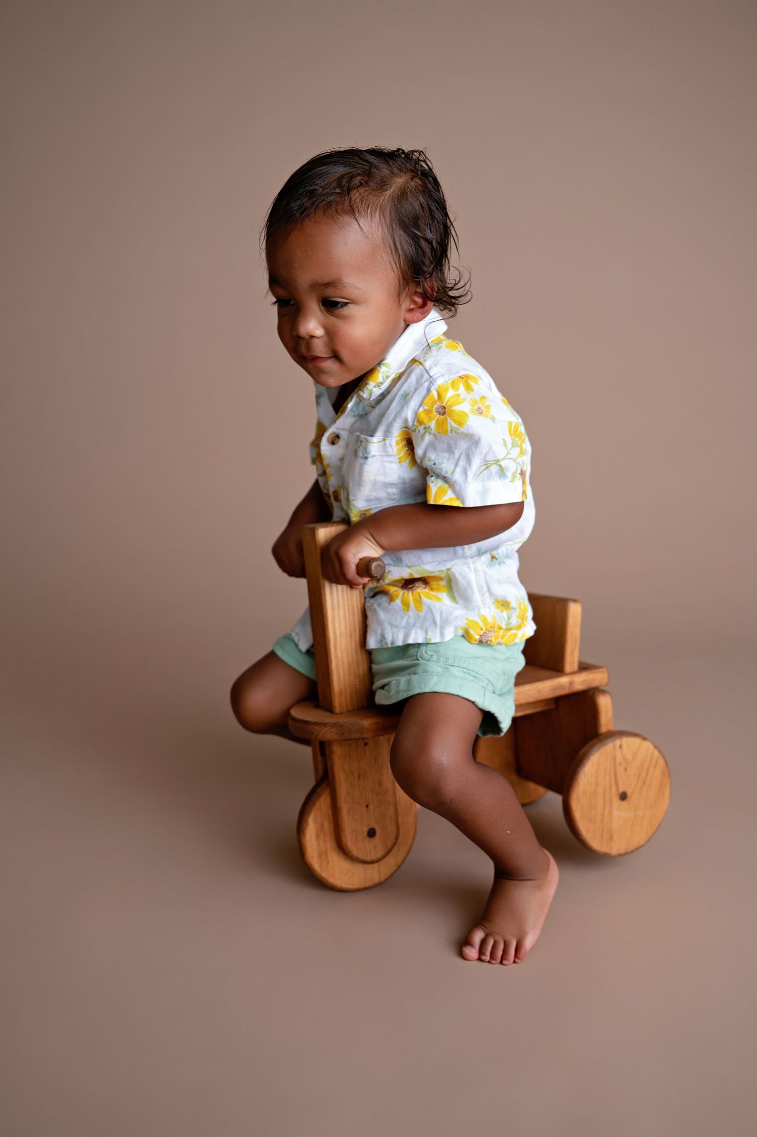 Baby in mint green outfit plays on wooden rocking toy against beige backdrop.