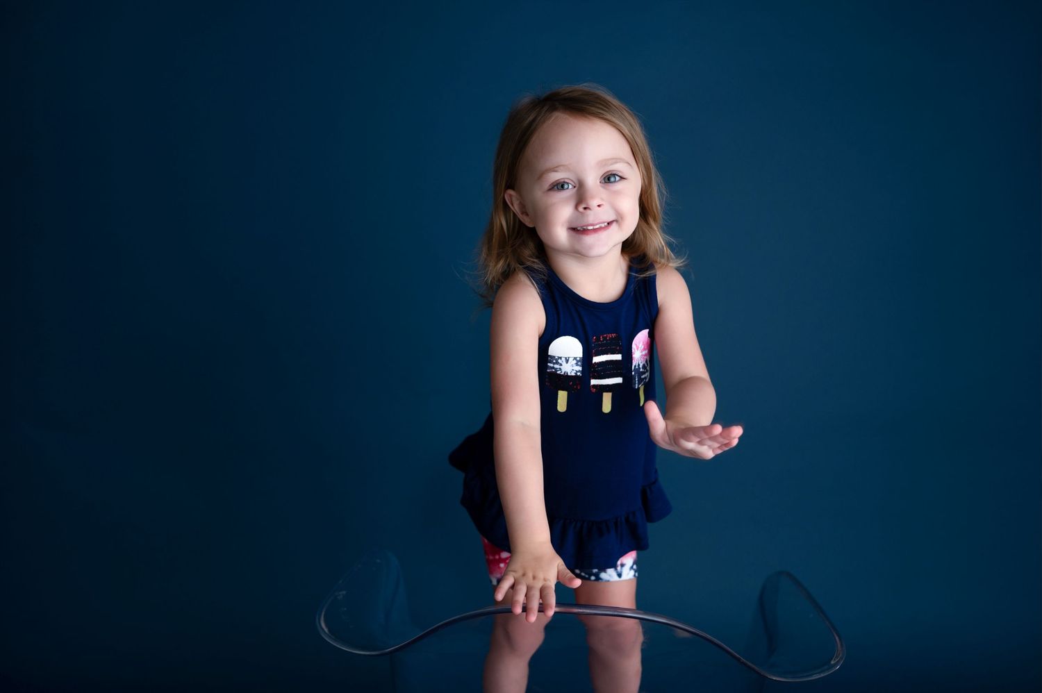 Young child in navy blue outfit sits against dark background with arms outstretched.