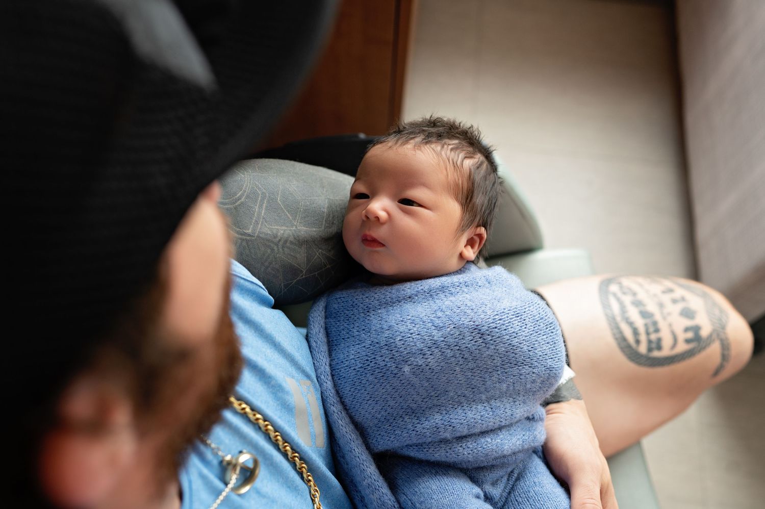 A newborn baby wrapped in a soft blue blanket rests peacefully on someone's lap.