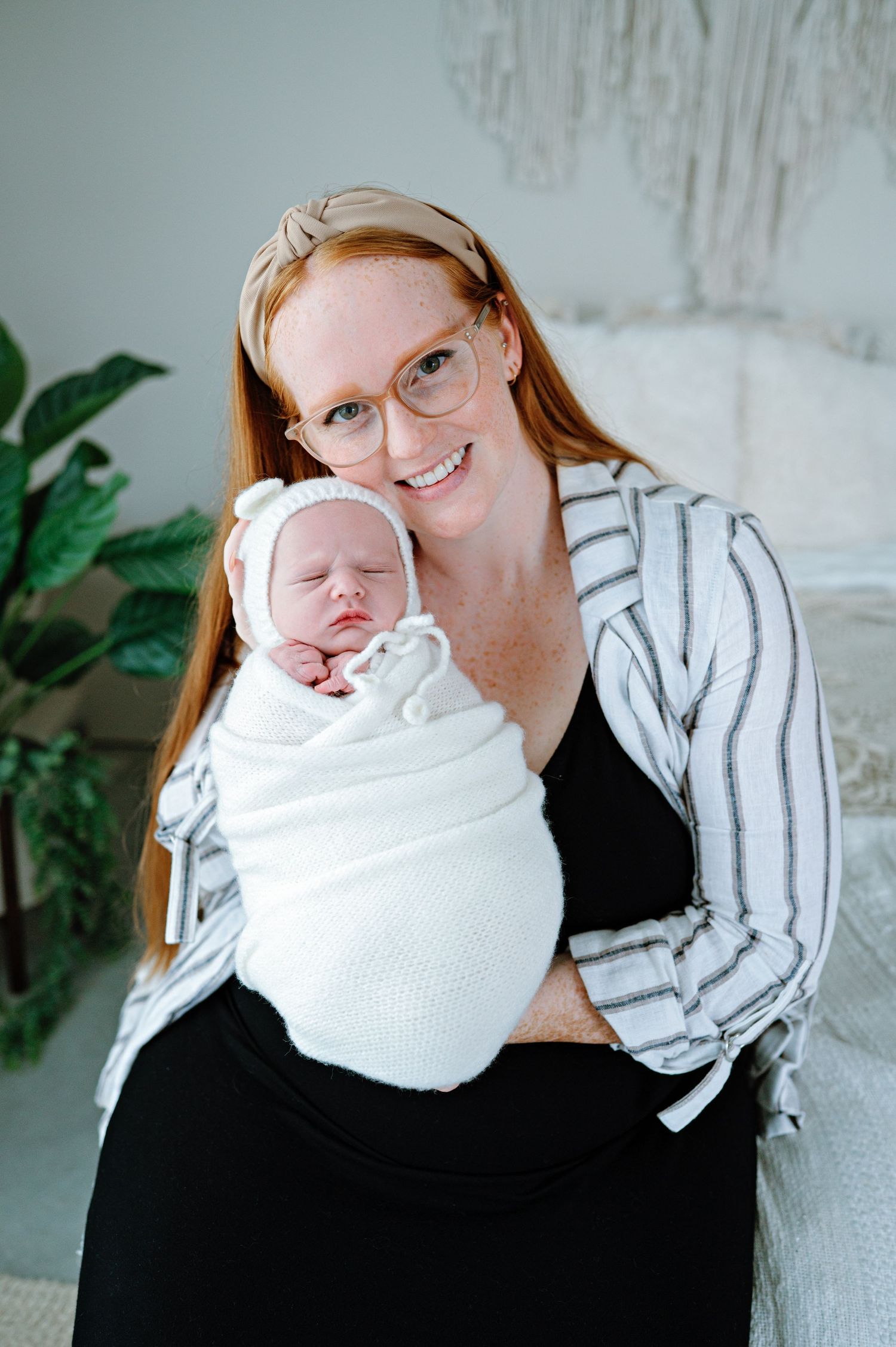Woman in striped cardigan holding swaddled newborn in bright modern nursery setting.
