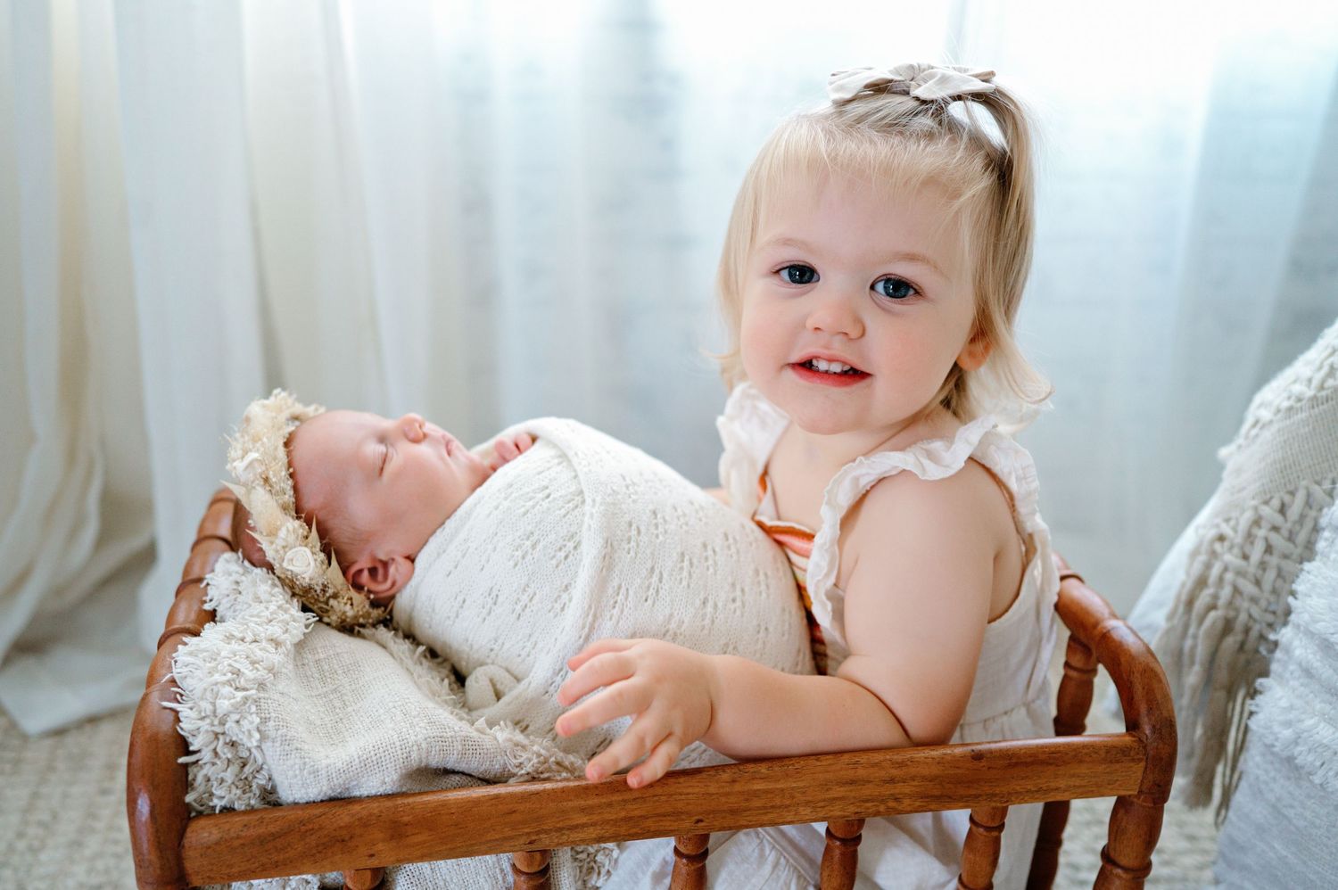 Two young children sharing a tender moment together in a wooden crib with a light curtain backdrop.