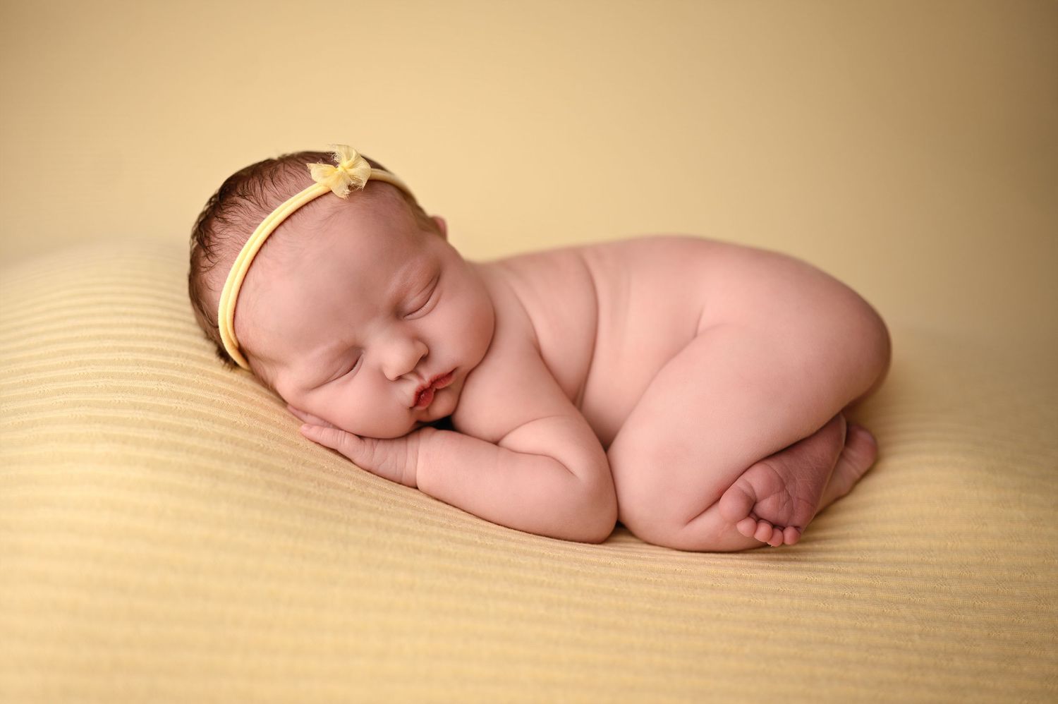 Sleeping newborn baby lying on soft beige textured blanket in warm lighting.