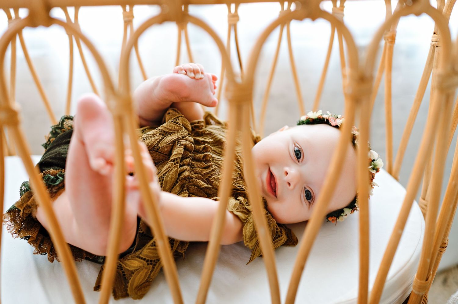 Baby laying in a woven rattan chair wearing mustard yellow clothing with a sweet expression.