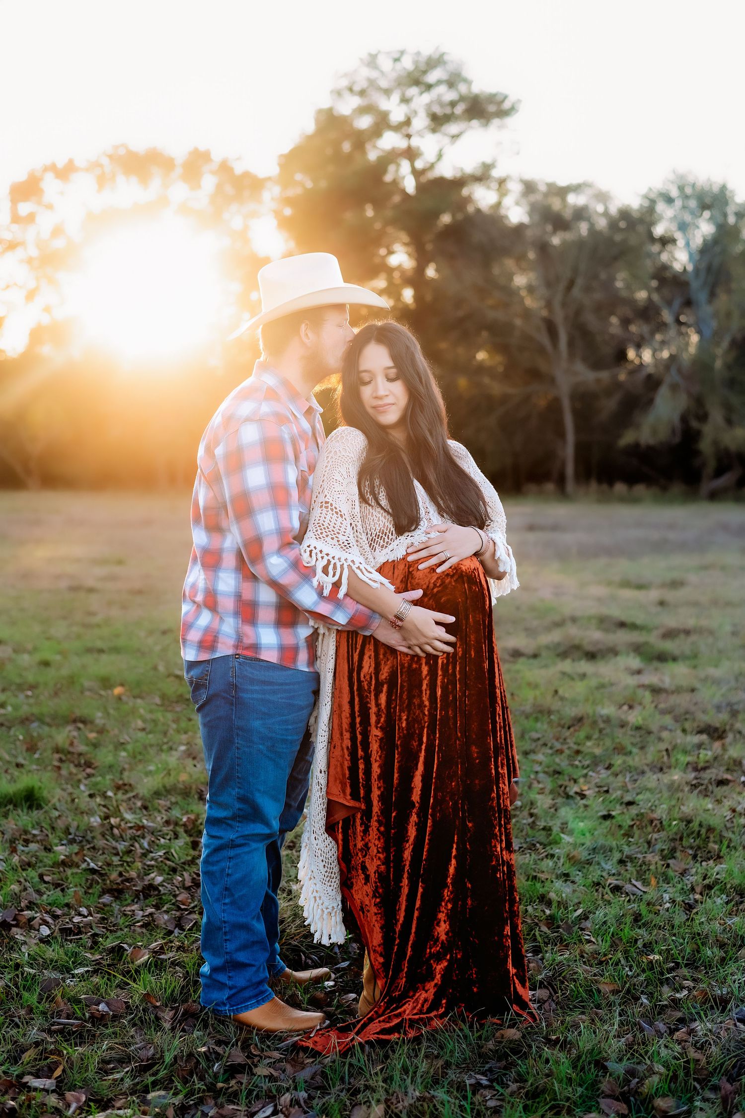 Sunset maternity photoshoot in a field with warm golden light and rich burgundy velvet dress.