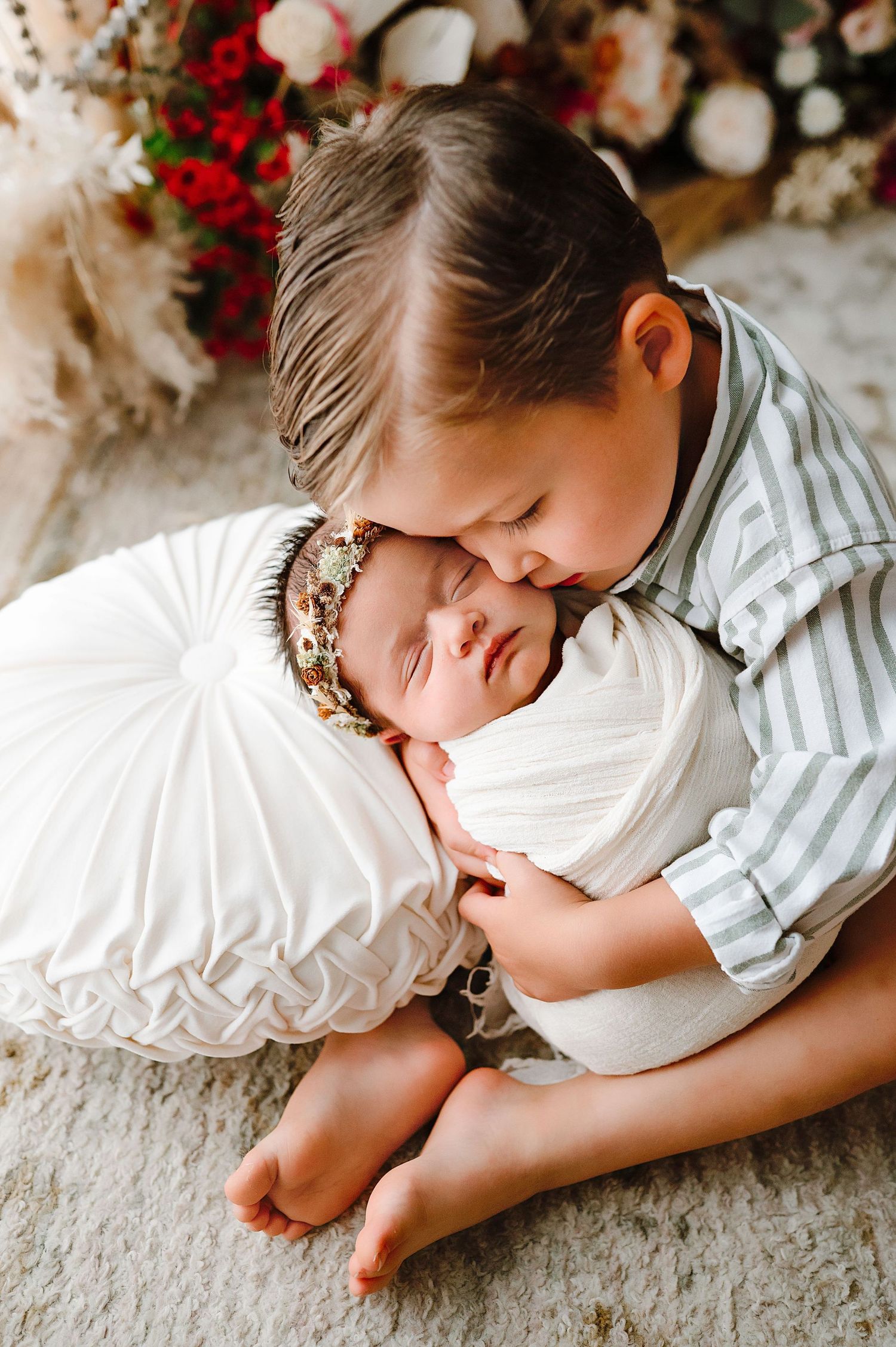 A sweet moment of an older sibling gently embracing a sleeping newborn on a carpeted floor.