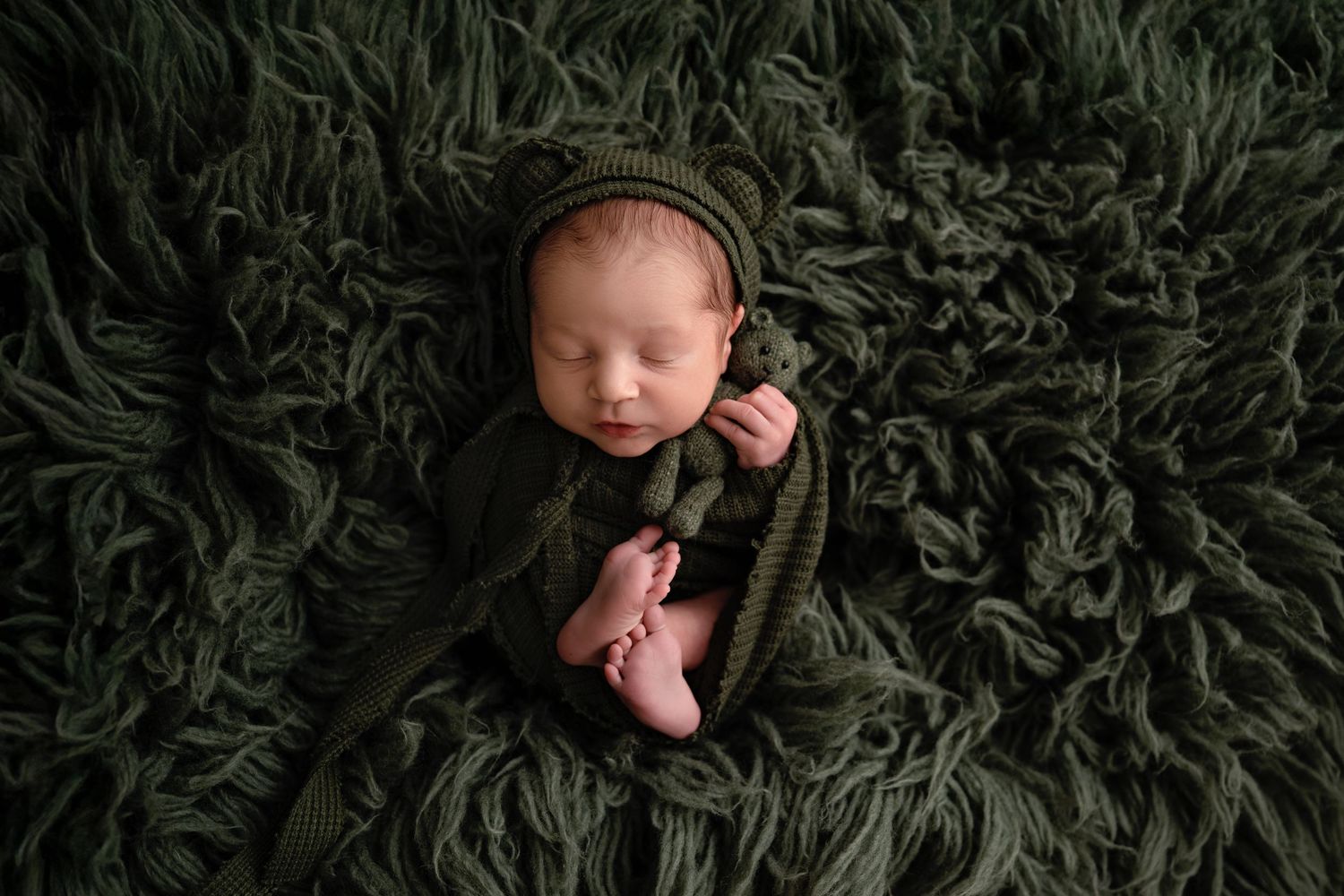 A collection of artistic newborn photography shots featuring a sleeping baby on dark green furry backdrop.
