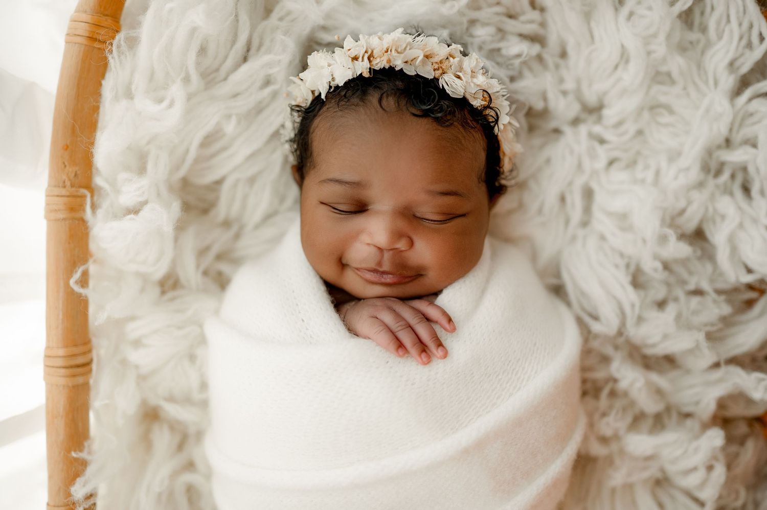 A sleeping newborn baby swaddled in white blankets and lace rests peacefully on a textured white background.