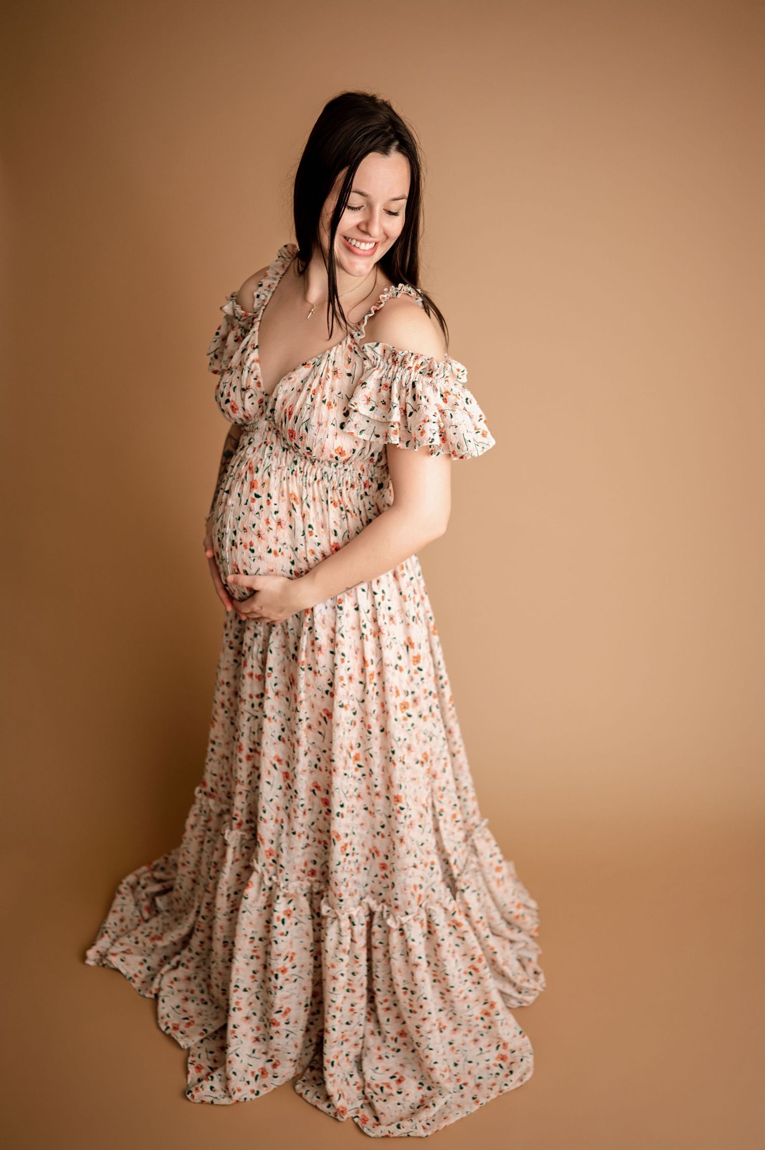 A flowy floral dress is showcased in multiple poses against a warm brown studio backdrop.