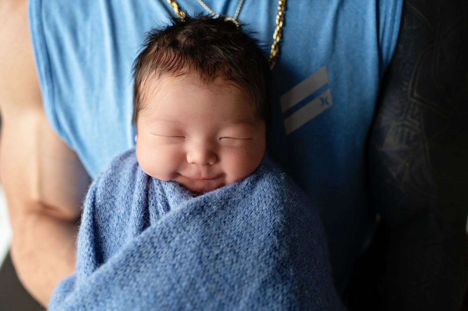 Peaceful sleeping newborn baby wrapped in soft blue knit blanket smiles while being held.