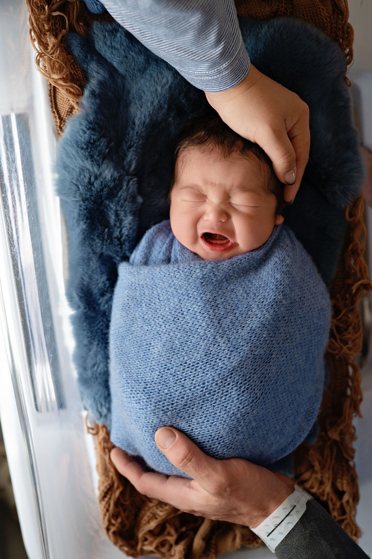 A sleeping newborn baby swaddled in a blue knit blanket rests peacefully in a woven basket.