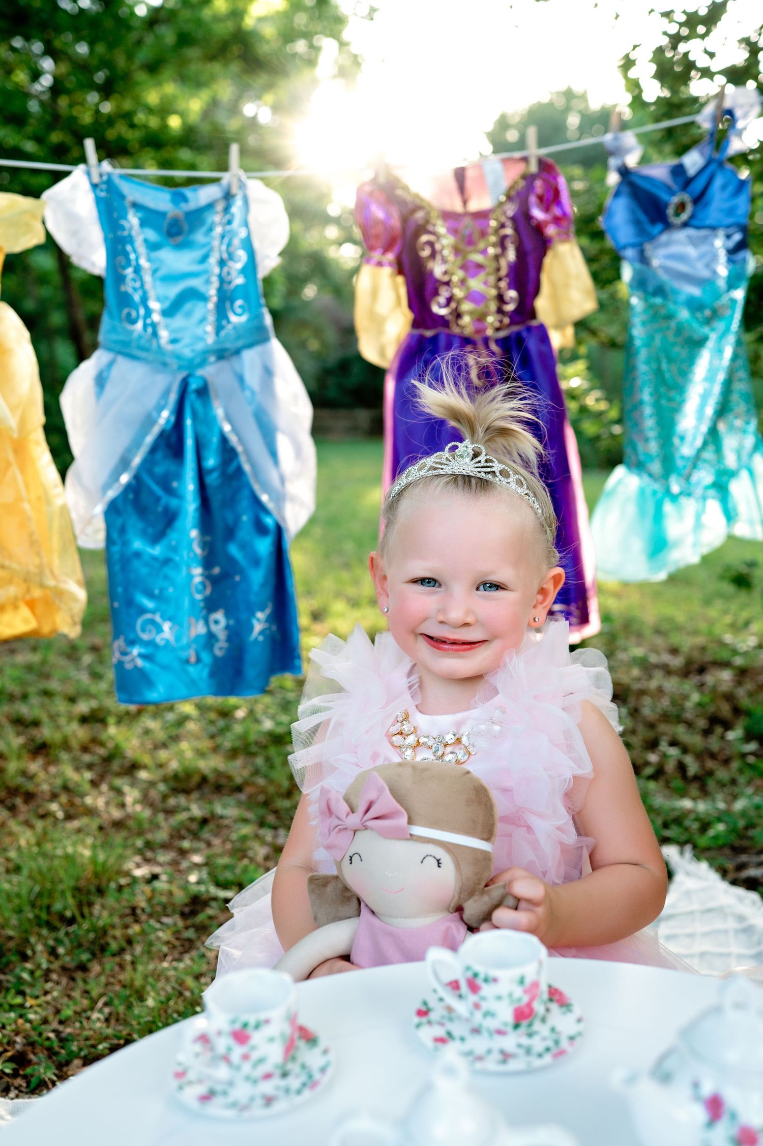 Tea party setup outdoors with princess dresses hanging on clothesline in background.