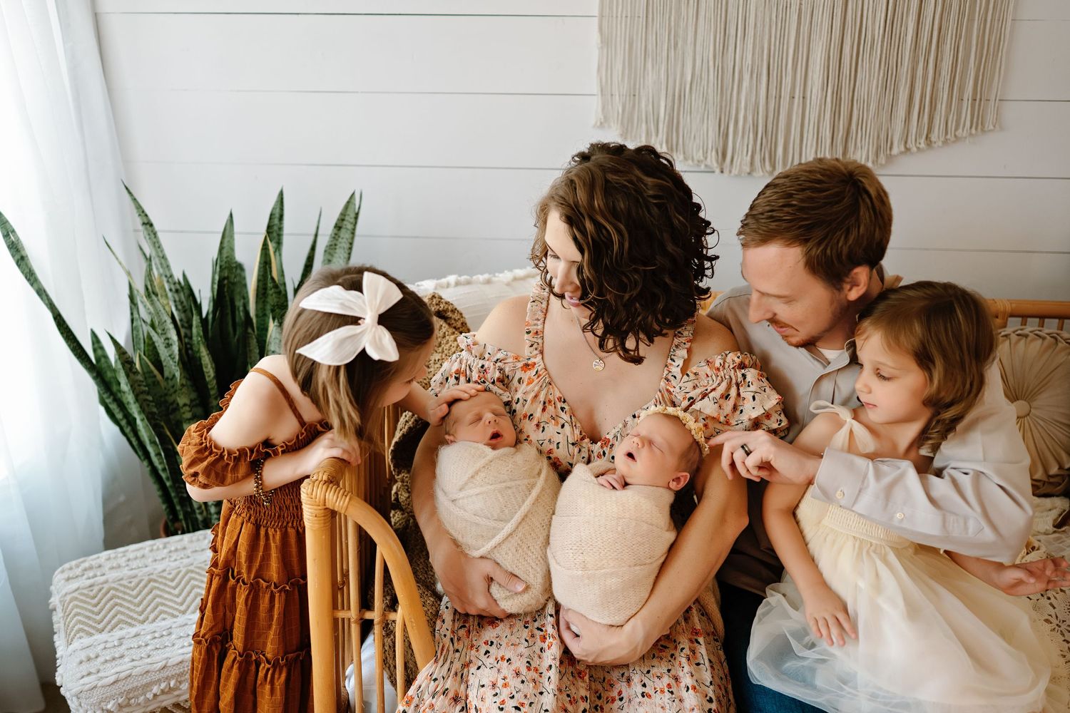 A family sits together on a couch wearing earth-toned clothing with a snake plant in the background.