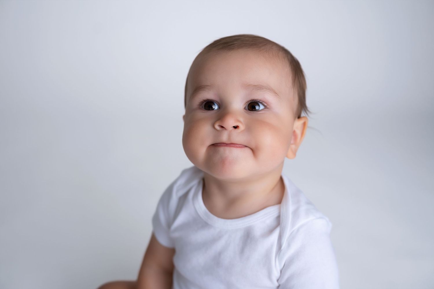 Baby in simple white outfit against clean white studio background.