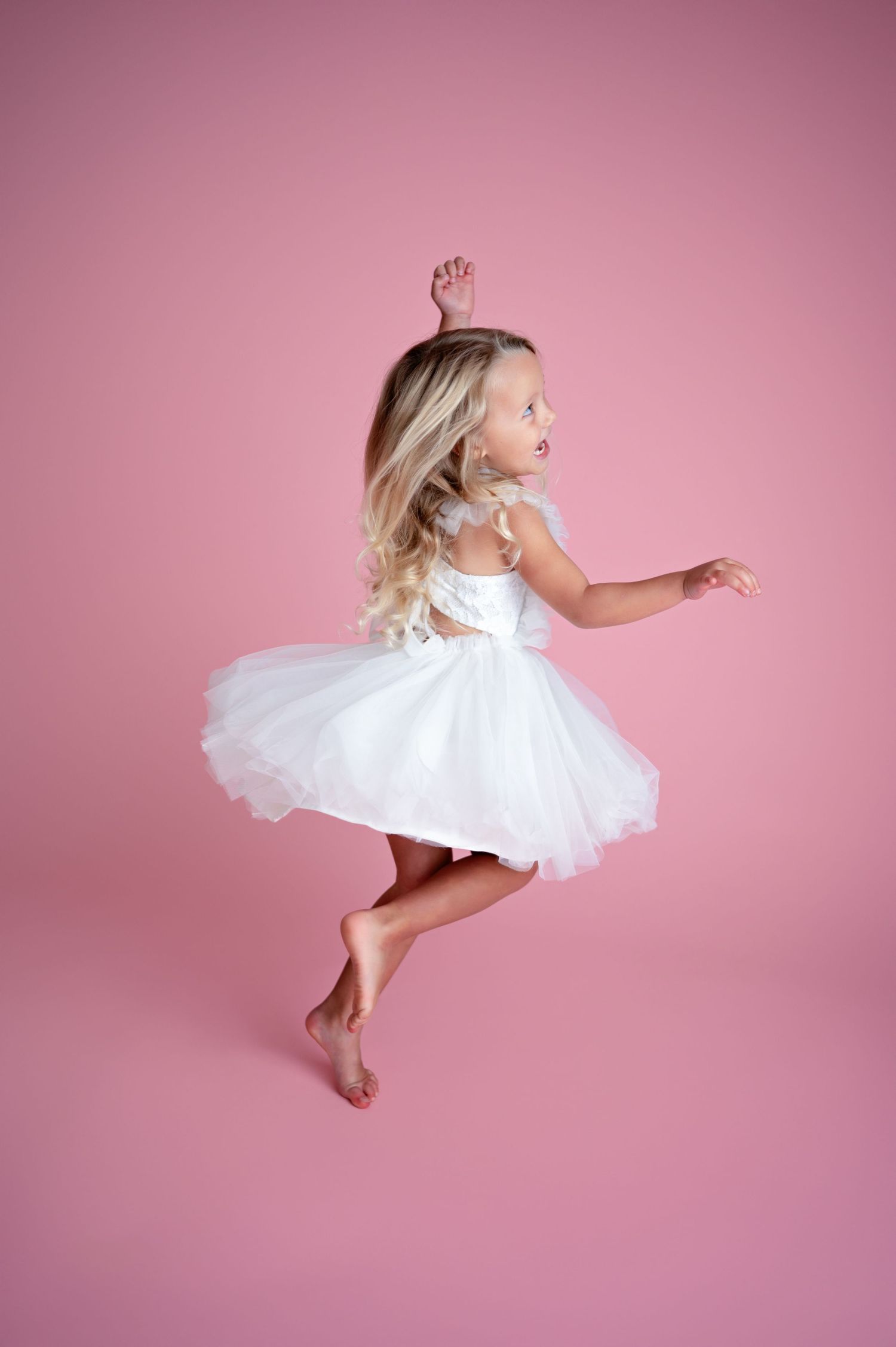A barefoot dancer in a white tutu leaps gracefully against a pink studio backdrop in a dynamic series of poses.