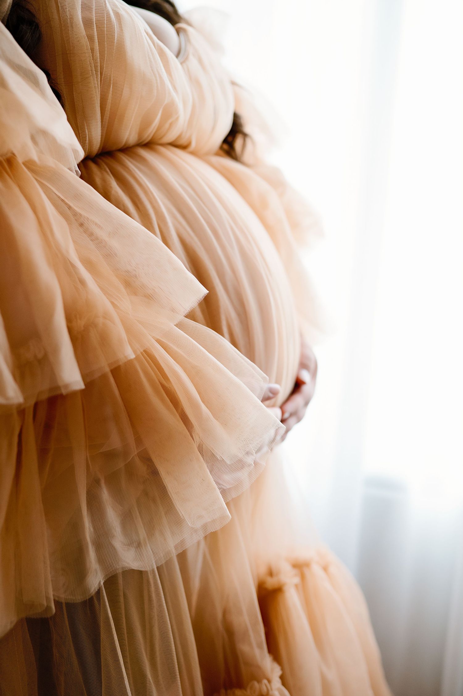 Detail shot of peachy tulle maternity gown fabric and baby bump.