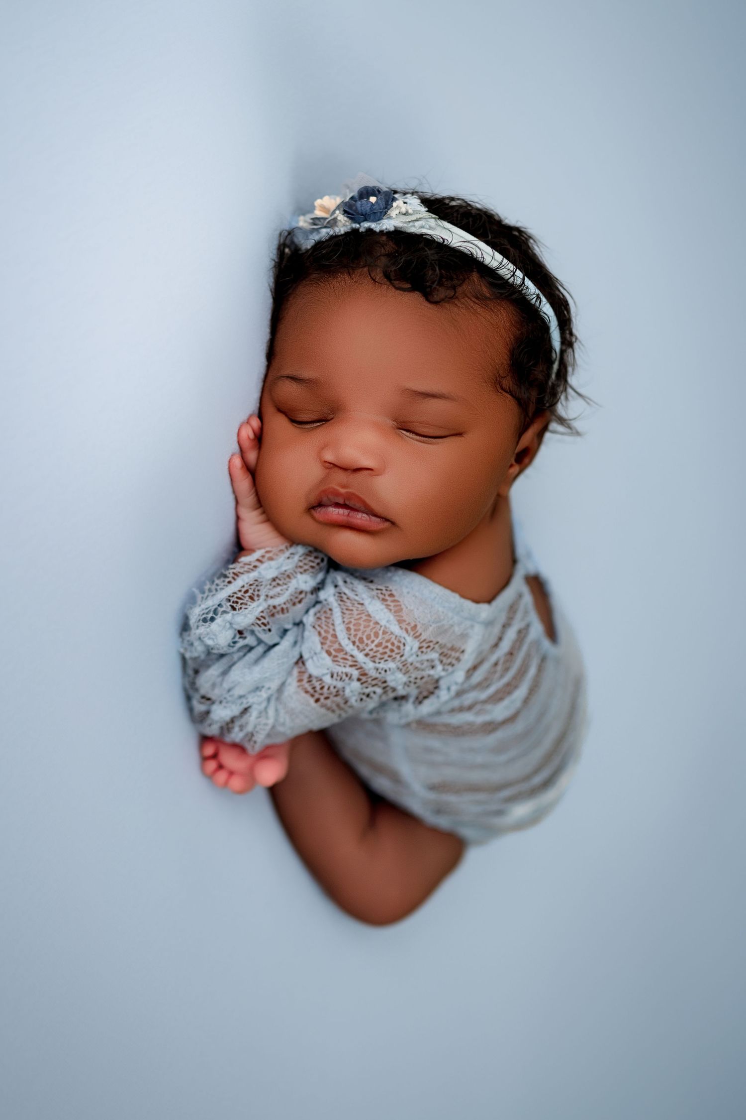 Peaceful sleeping newborn wearing soft gray wrap in dreamy blue-tinted portrait series.