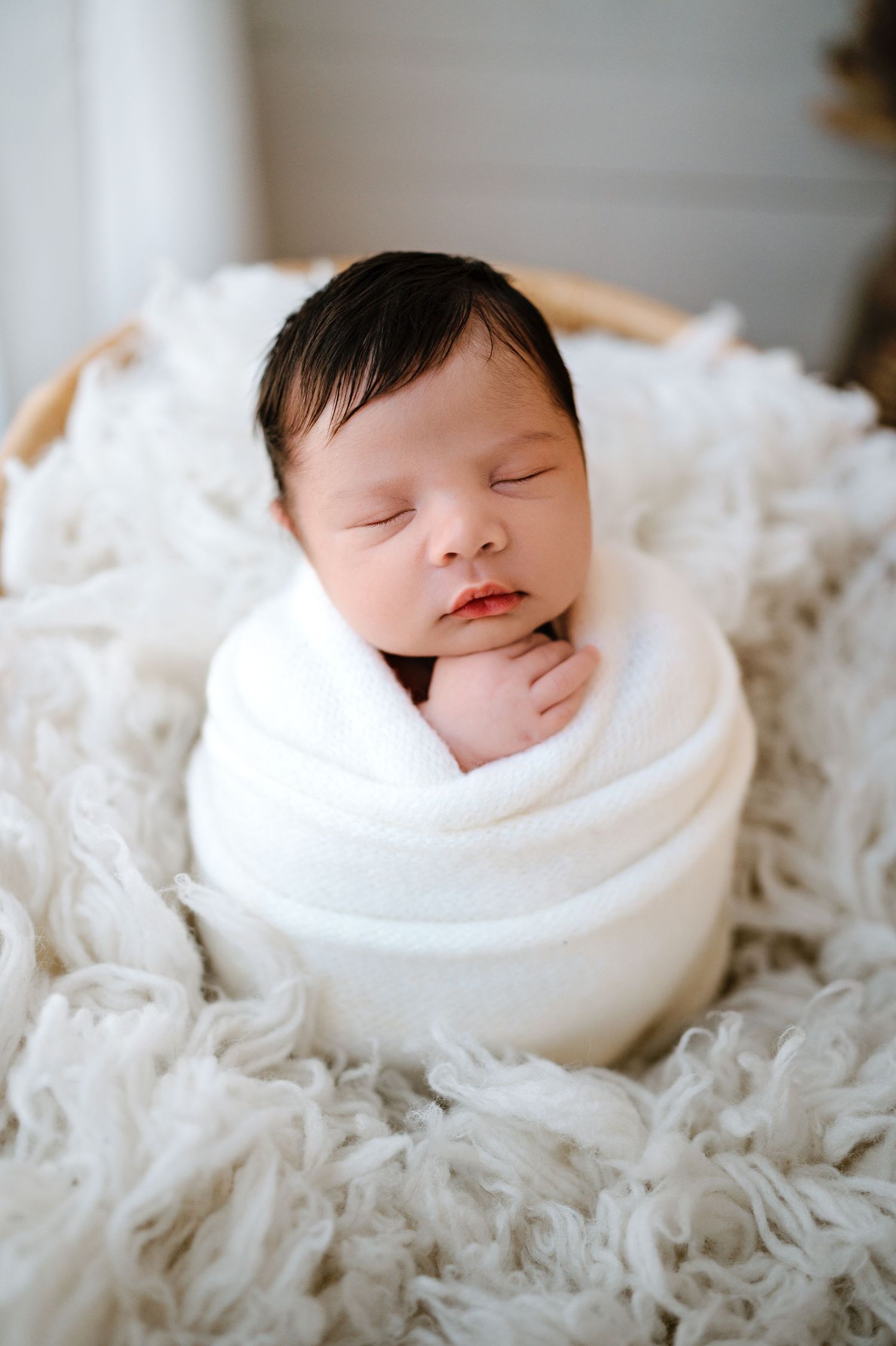 Peaceful sleeping newborn baby swaddled in white fabric nestled in soft textured blankets.
