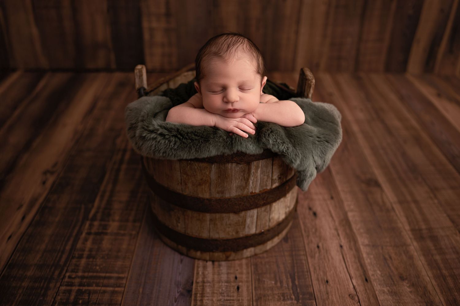 A series of six photos showing a baby in a rustic wooden barrel prop against a dark wooden floor background.