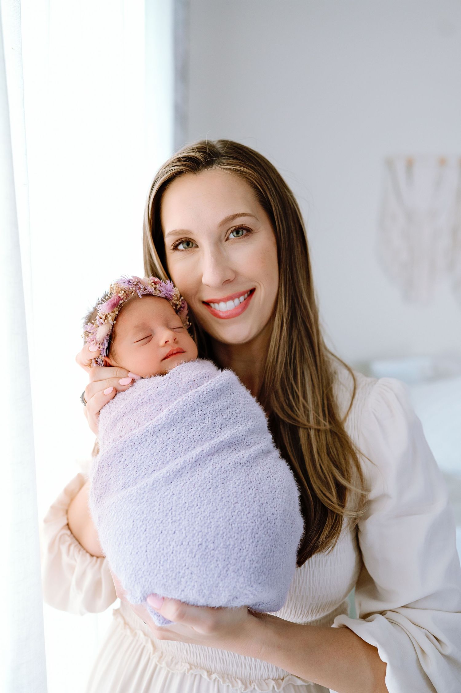 Parent in cream sweater holding sleeping newborn wrapped in soft purple blanket.