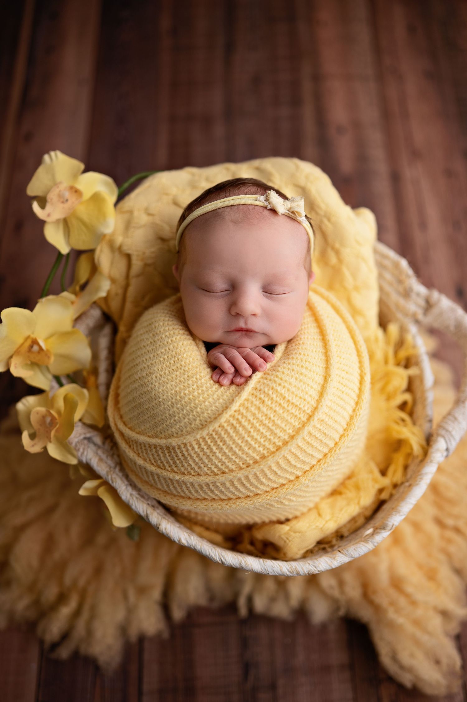 A sleeping newborn wrapped in soft yellow knit blankets with daffodils, photographed in a series of peaceful poses.