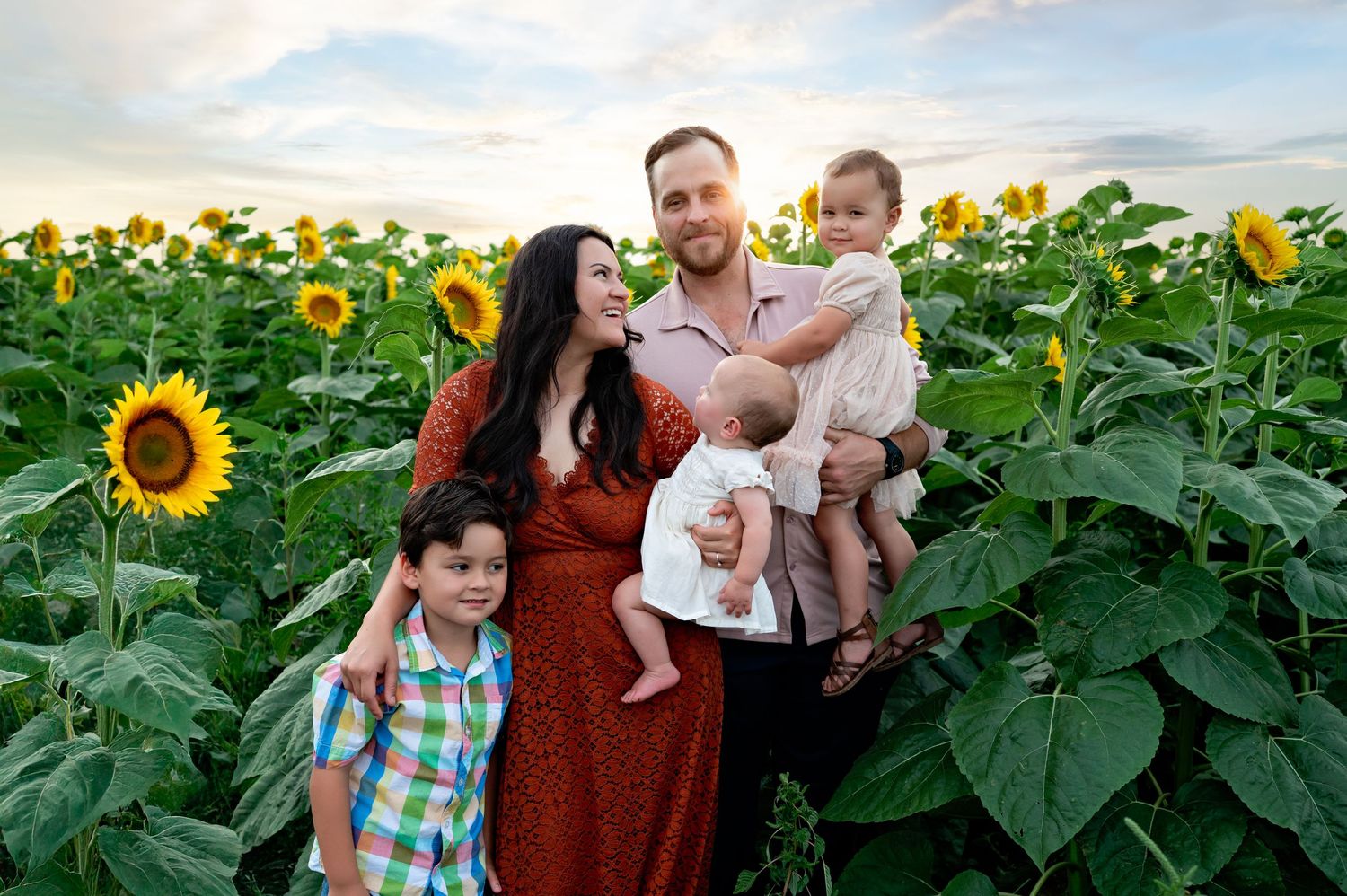 Family photoshoot in vibrant sunflower field during golden hour.