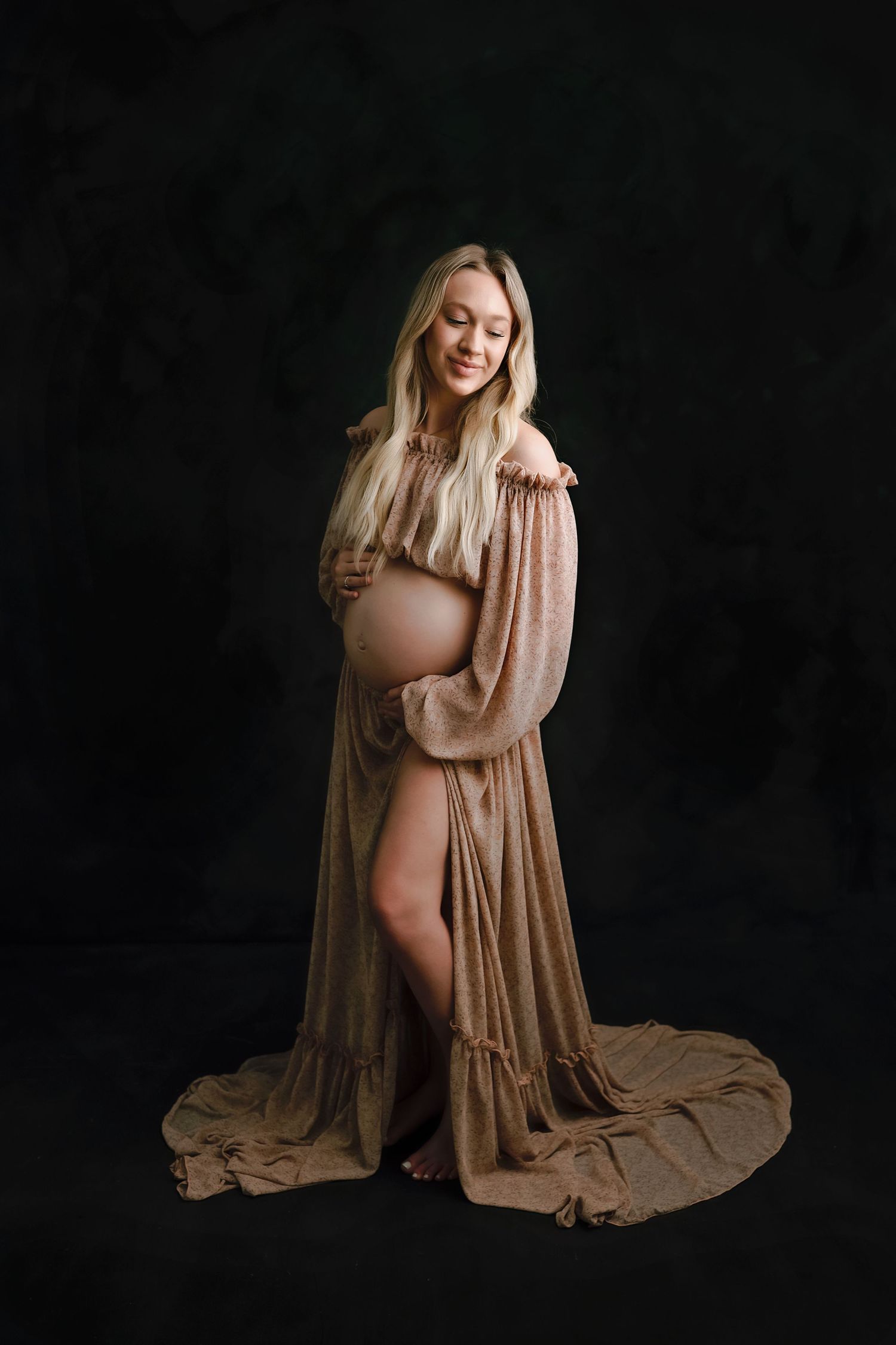 Artistic maternity photography with flowing fabric against dark background.