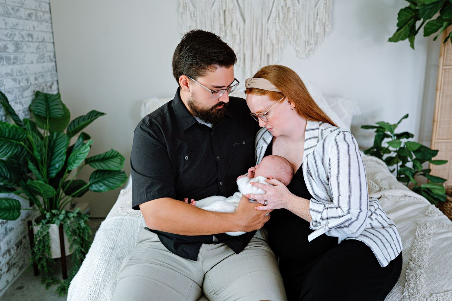 Family sharing tender moments together on white bedding with greenery in background.