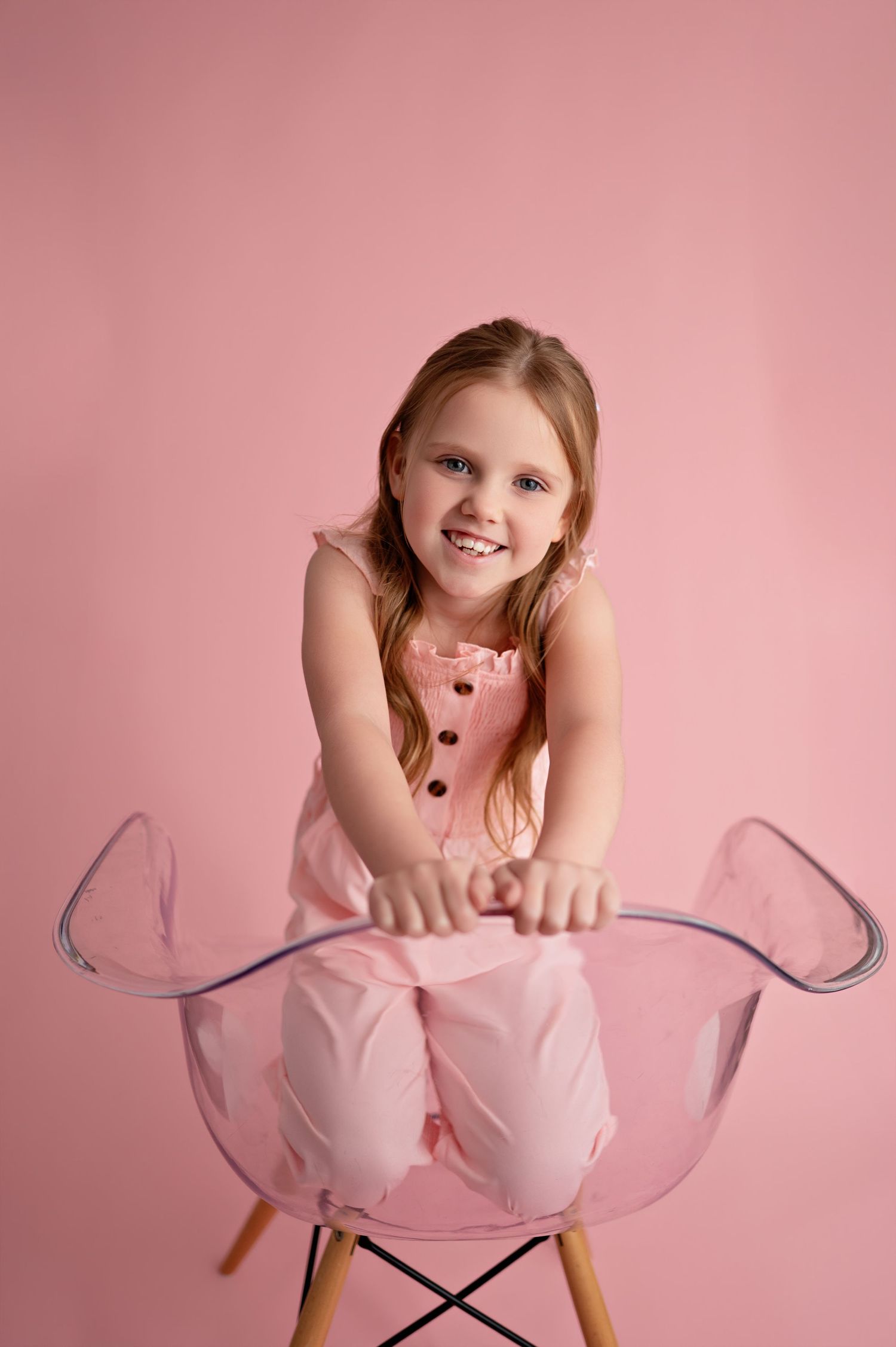 A child in a pink tutu dress poses playfully on a chair against a pink backdrop in a series of candid shots.