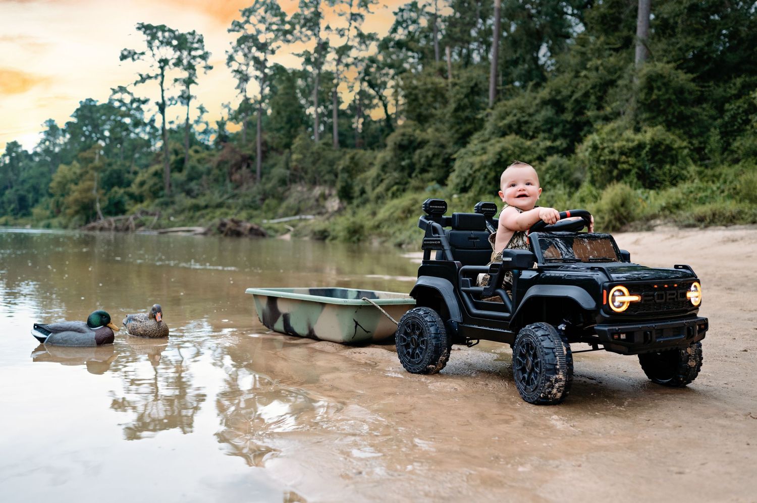 Black toy electric ride-on Jeep parked on sandy beach near water with ducks swimming at sunset.