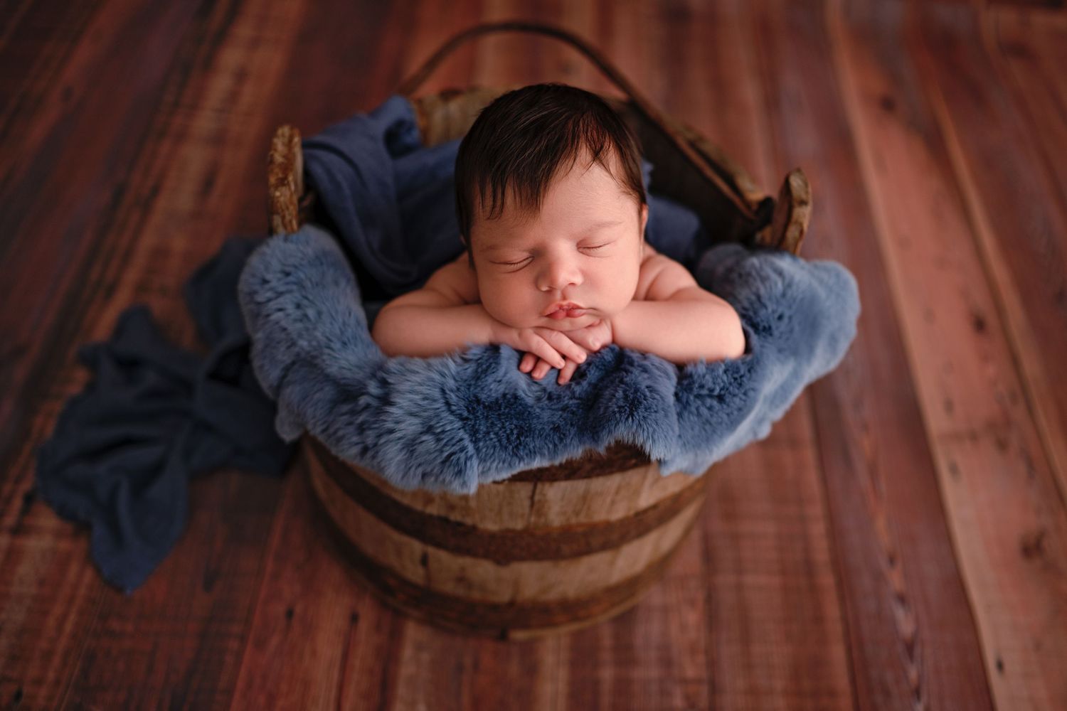 Sleeping newborn baby posed in blue wrap on wooden floor with multiple artistic angles captured.
