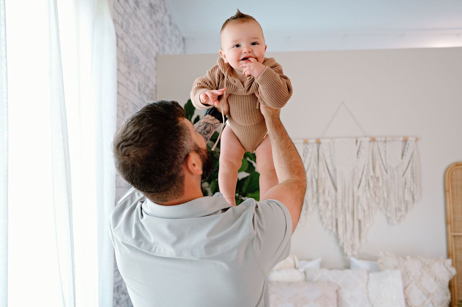 A parent and baby interact playfully together while lying on a couch at home.