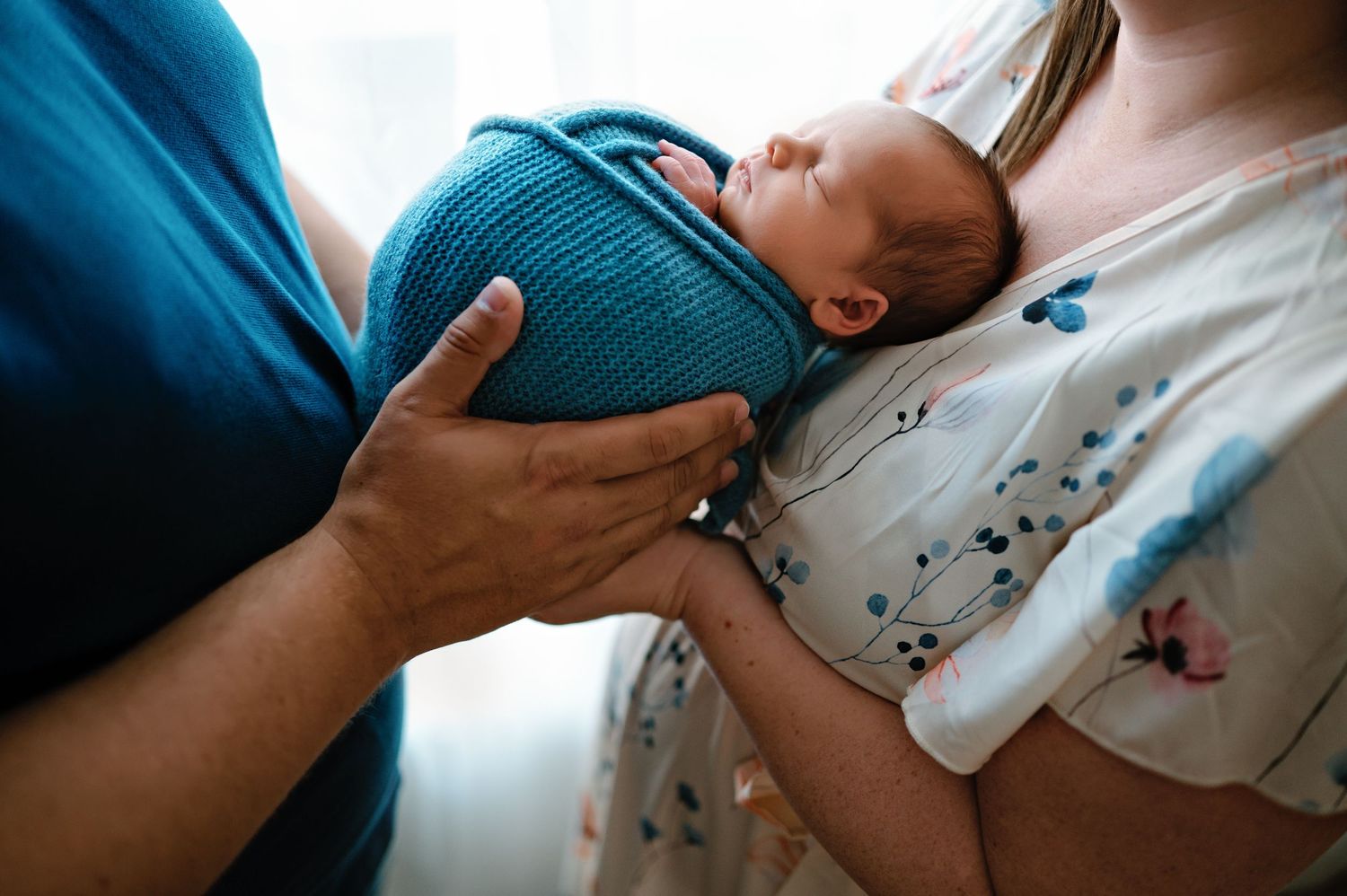 Newborn baby swaddled in teal blanket cradled in mother's arms during tender postpartum moment.