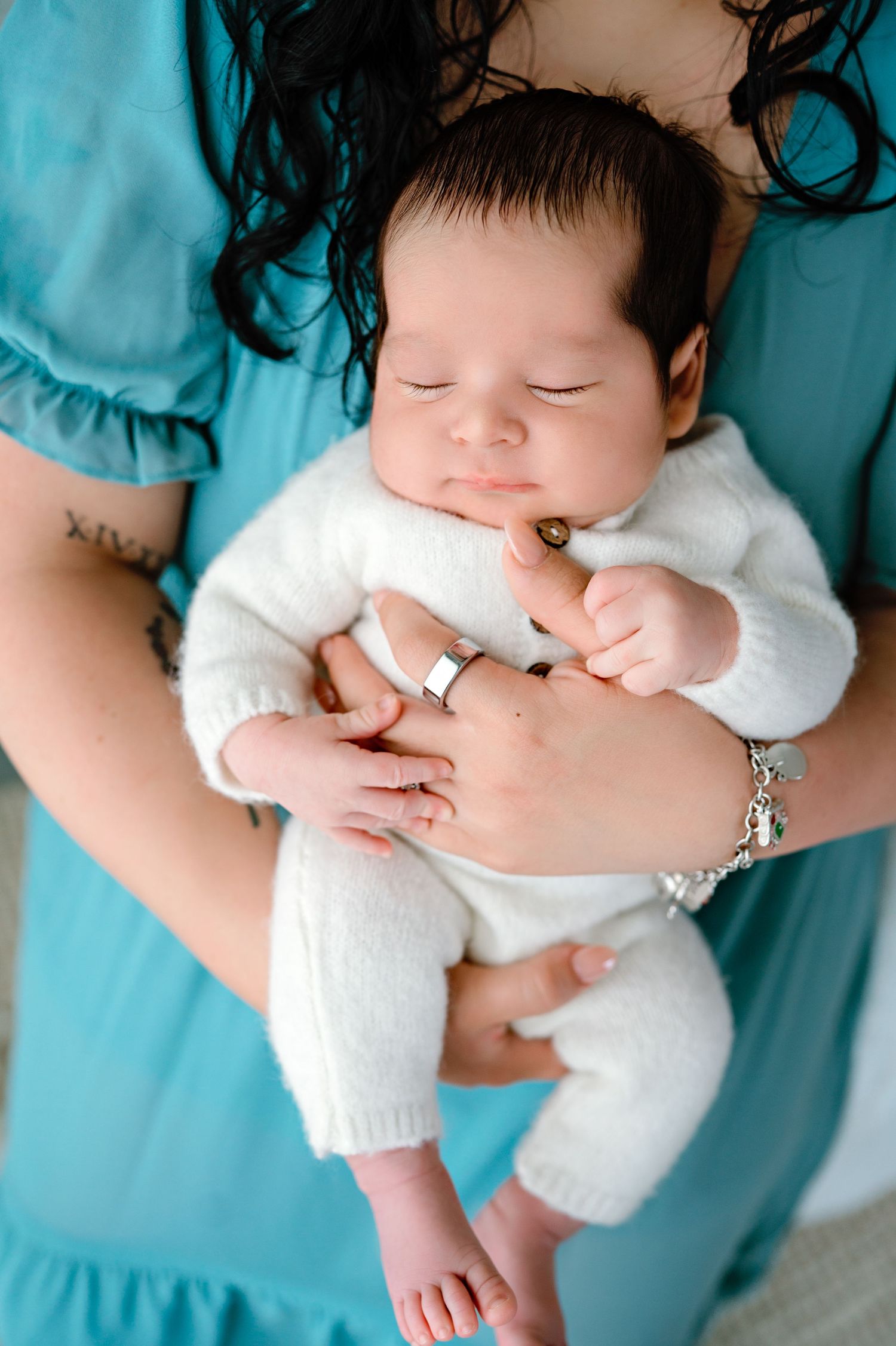 Peaceful sleeping newborn in white outfit cradled in turquoise fabric.