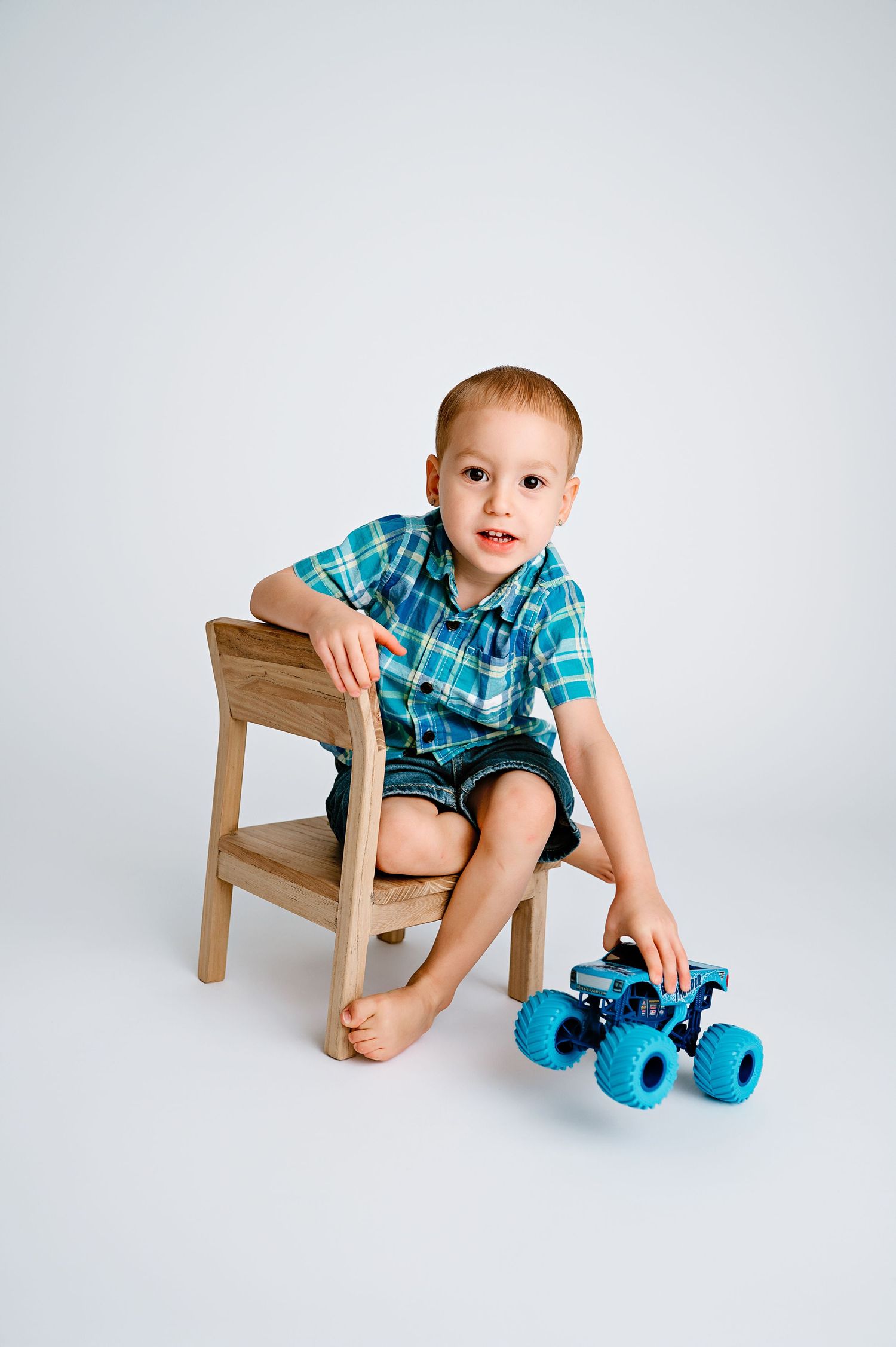 A young child in plaid shirt sits on wooden chair with blue roller skates.