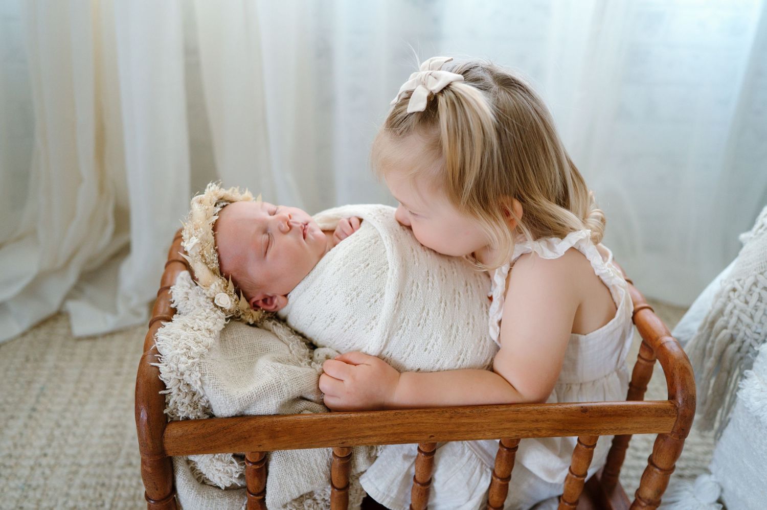 Professional photograph of a baby sleeping peacefully on a wooden bench with white bedding and delicate details.