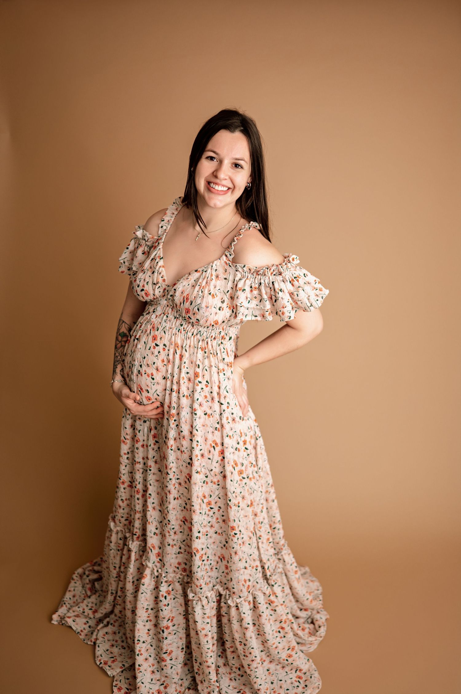 A floral maxi dress with ruffled details is modeled against a neutral brown background.