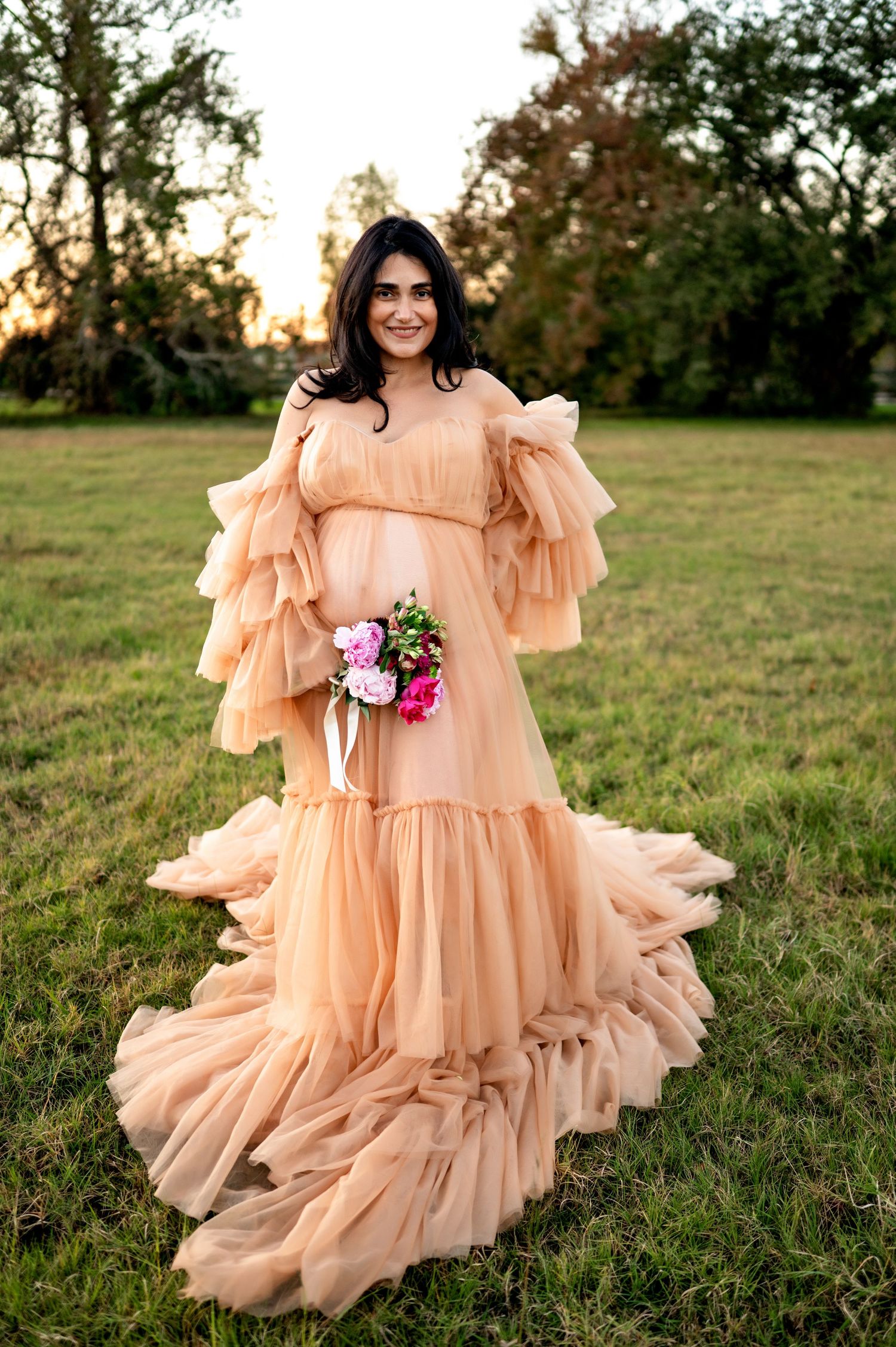 A flowing peach-colored ruffle dress with balloon sleeves twirls in a grassy field at sunset.