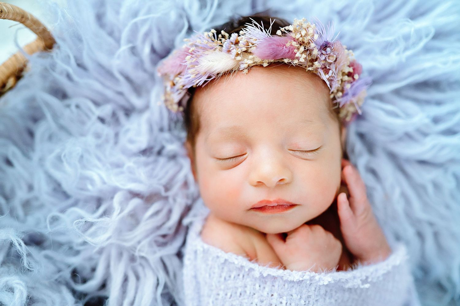 Sleeping newborn with delicate floral crown against soft blue background.