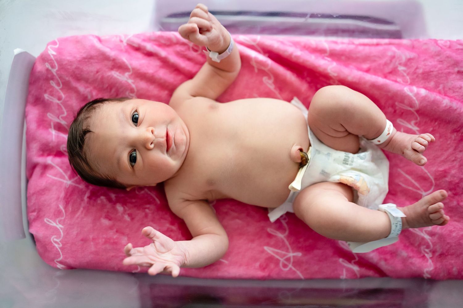 Newborn baby lying on soft pink velvet blanket during a professional photoshoot.