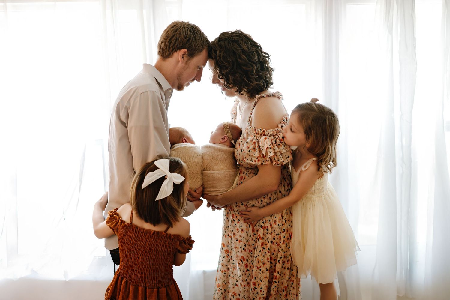 A family shares an intimate moment together in a bright sunlit room with white curtains.