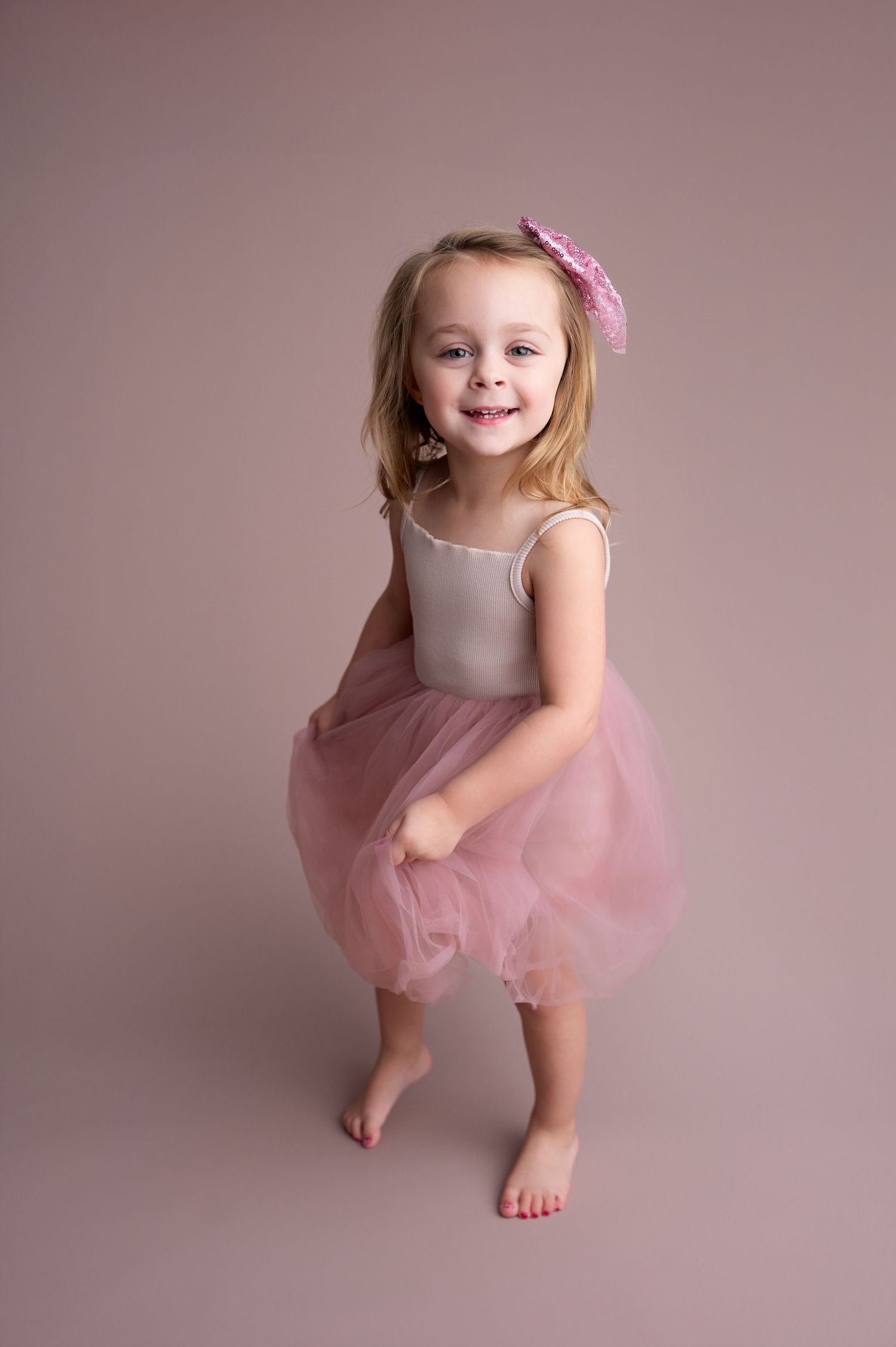 Young dancer in pink tutu and leotard performs graceful poses against neutral studio backdrop.