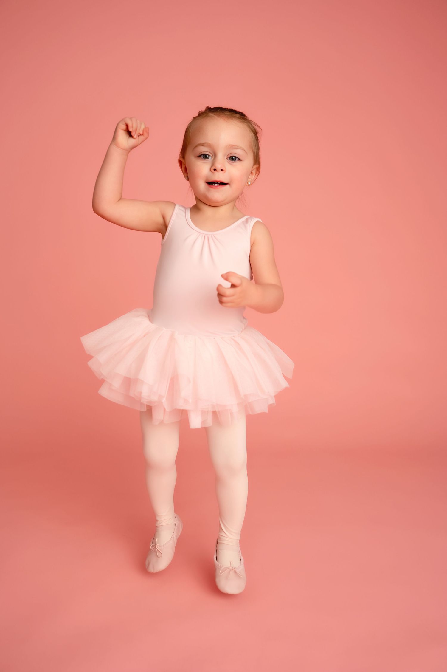Young dancer in pink tutu leaping and jumping against salmon colored background.
