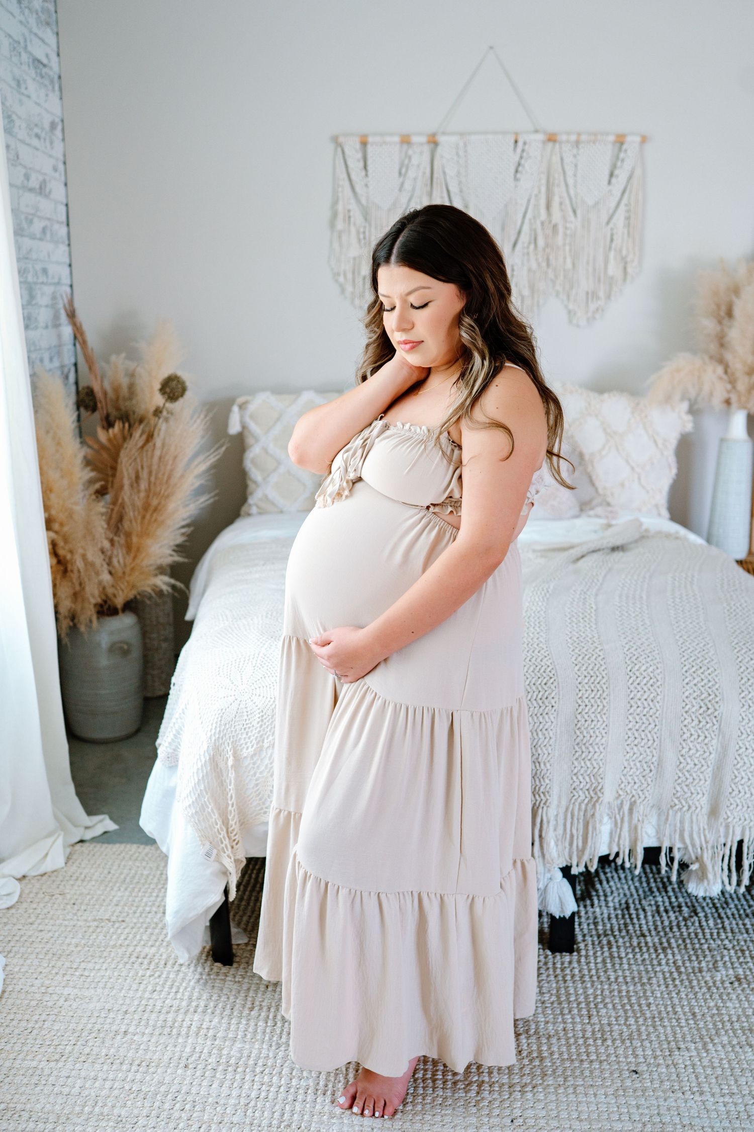 A maternity photoshoot series in a soft, bright bedroom featuring a white flowy dress and bohemian decor.