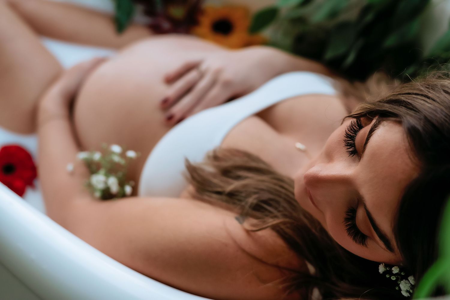 A romantic maternity milk bath portrait with delicate flowers and lush greenery.