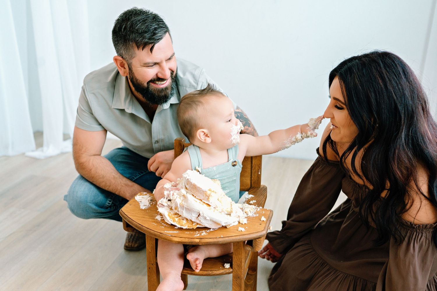 Family gathered around a smash cake during a first birthday celebration with string tassels and white decor.