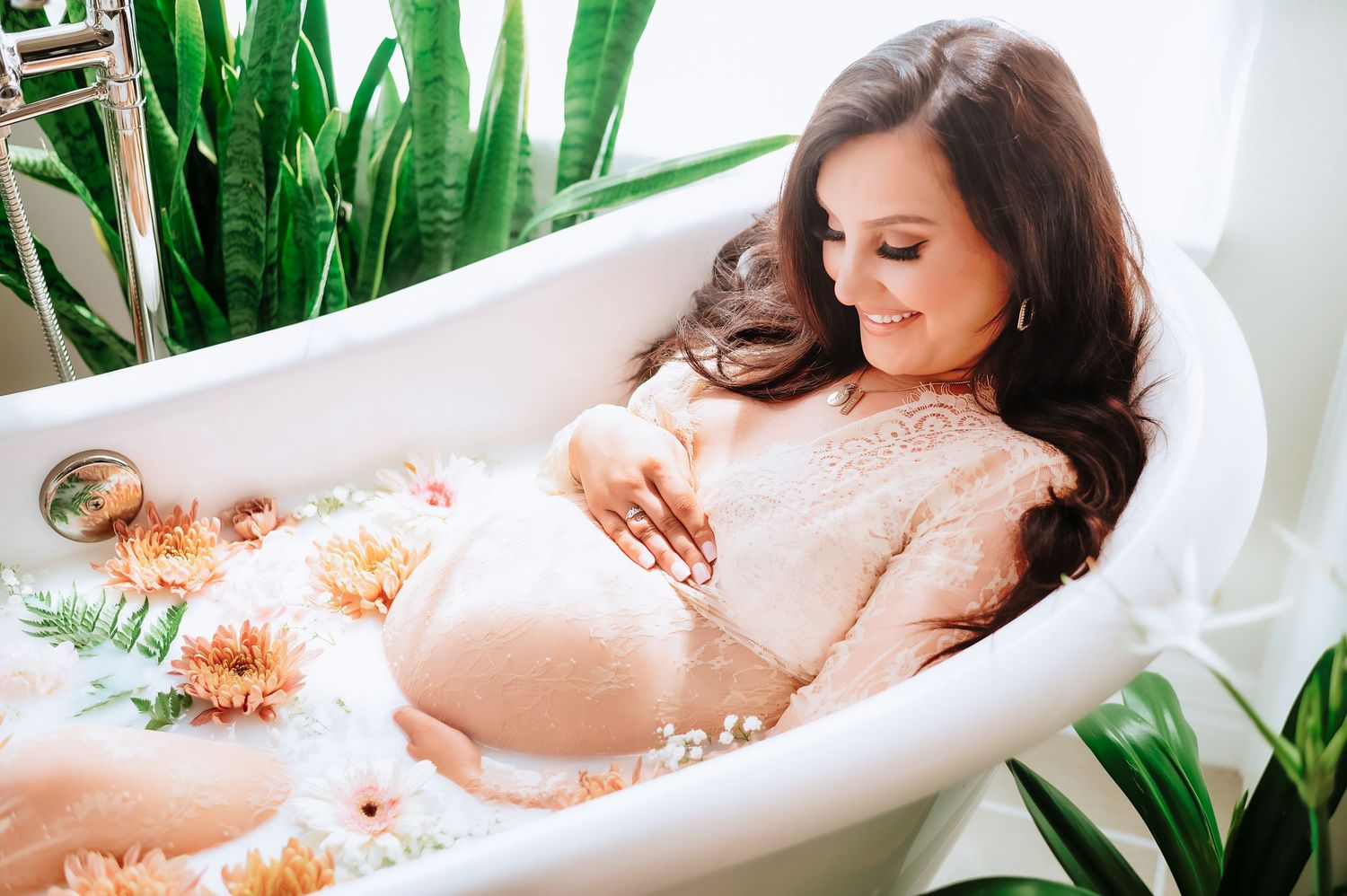 Bathtub filled with milk and citrus fruits surrounded by tropical green plants near bathroom window.